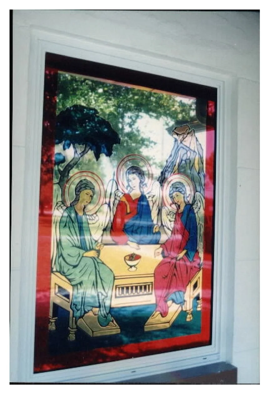 Religious stained glass window depicting three angels seated around a table with halos, in a peaceful outdoor setting with trees. colored window film