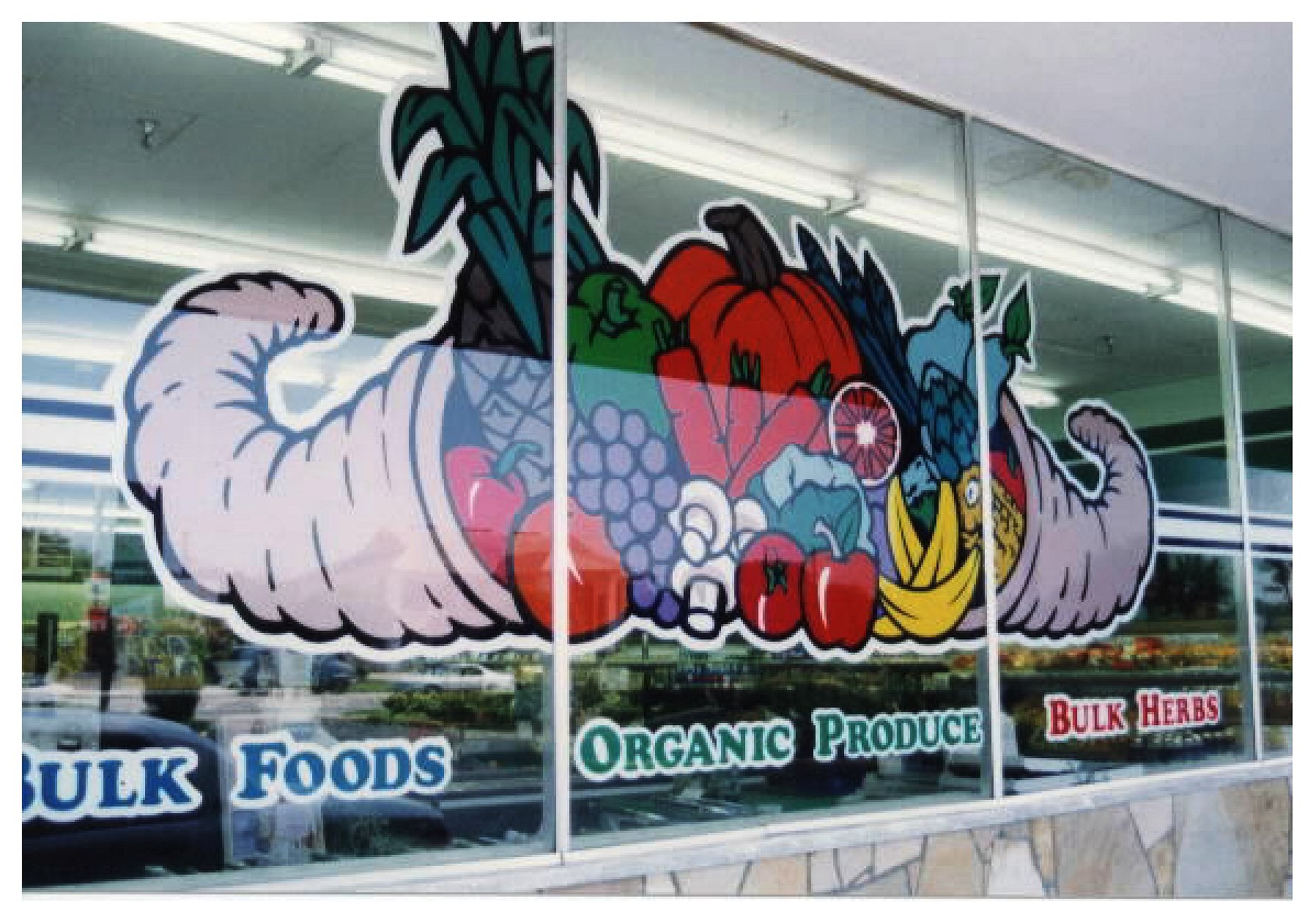 Colorful cornucopia graphic on store window featuring fruits and vegetables, with text 'Bulk Foods,' 'Organic Produce,' and 'Bulk Herbs' below. colored window film