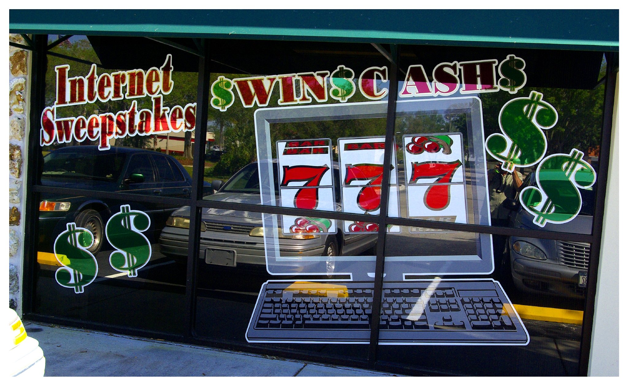 Storefront window advertising internet sweepstakes with slot machine graphics, dollar signs, and text promoting cash prizes. colored window film