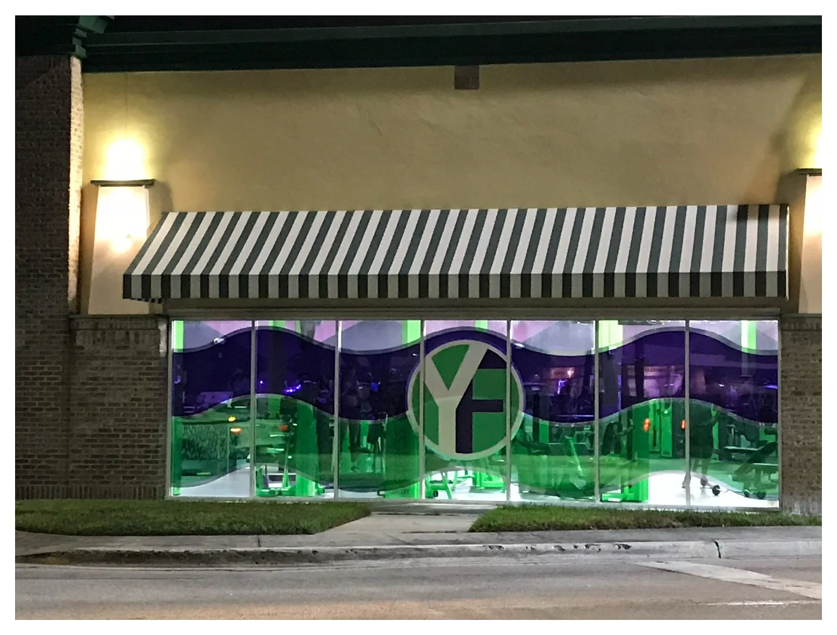 Exterior view of a storefront with a striped awning and large window with green and purple graphics. colored window film