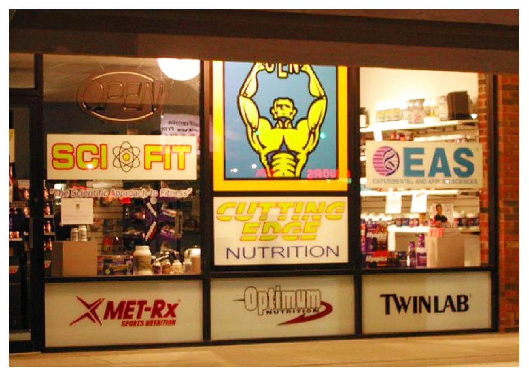 Supplement store window display with brand logos including Sci-Fit, Cutting Edge Nutrition, EAS, MET-Rx, Optimum Nutrition, and Twinlab. colored window film