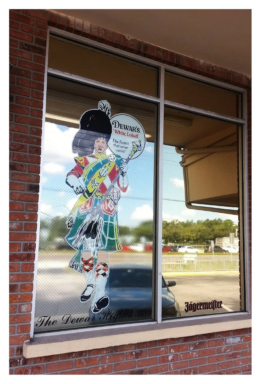 Window with Dewar's White Label advertisement depicting a Highlander and text promoting whiskey, alongside Jägermeister branding. colored window film