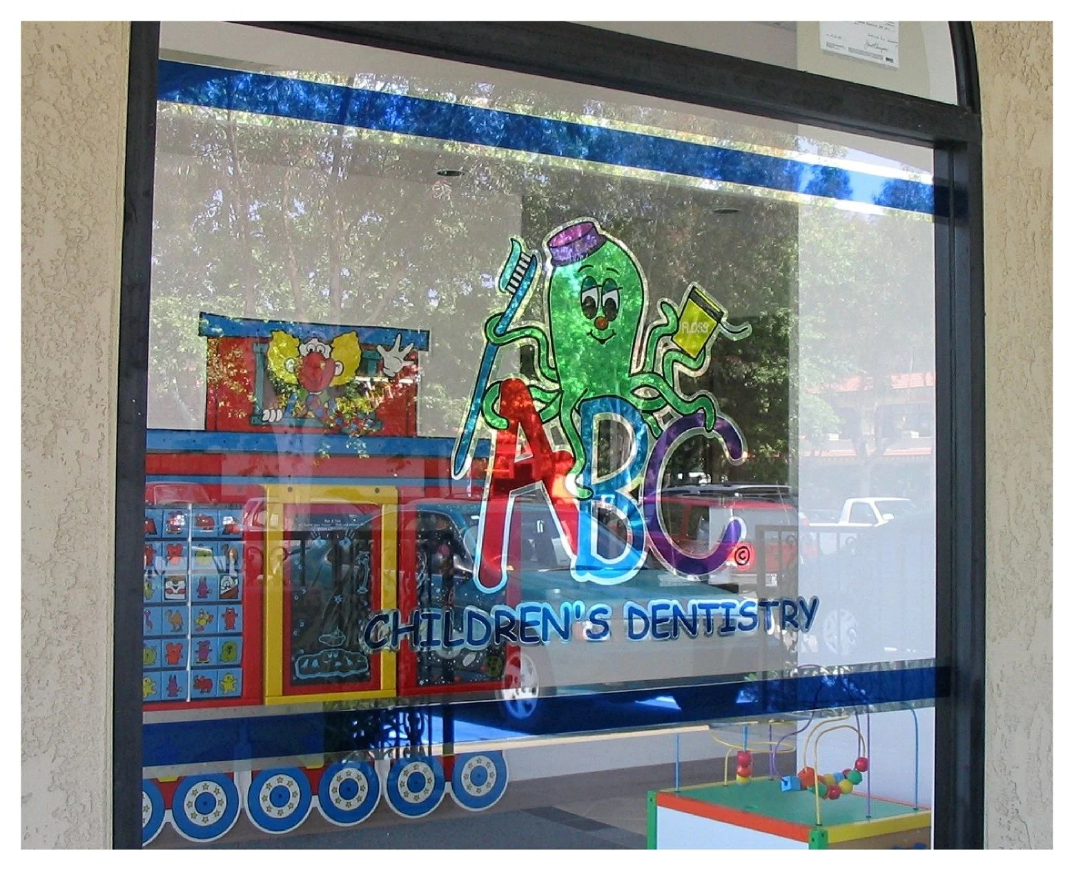 Colorful window display at children's dentistry with a cartoon octopus holding a toothbrush and floss, labeled "ABC Children's Dentistry." colored window film