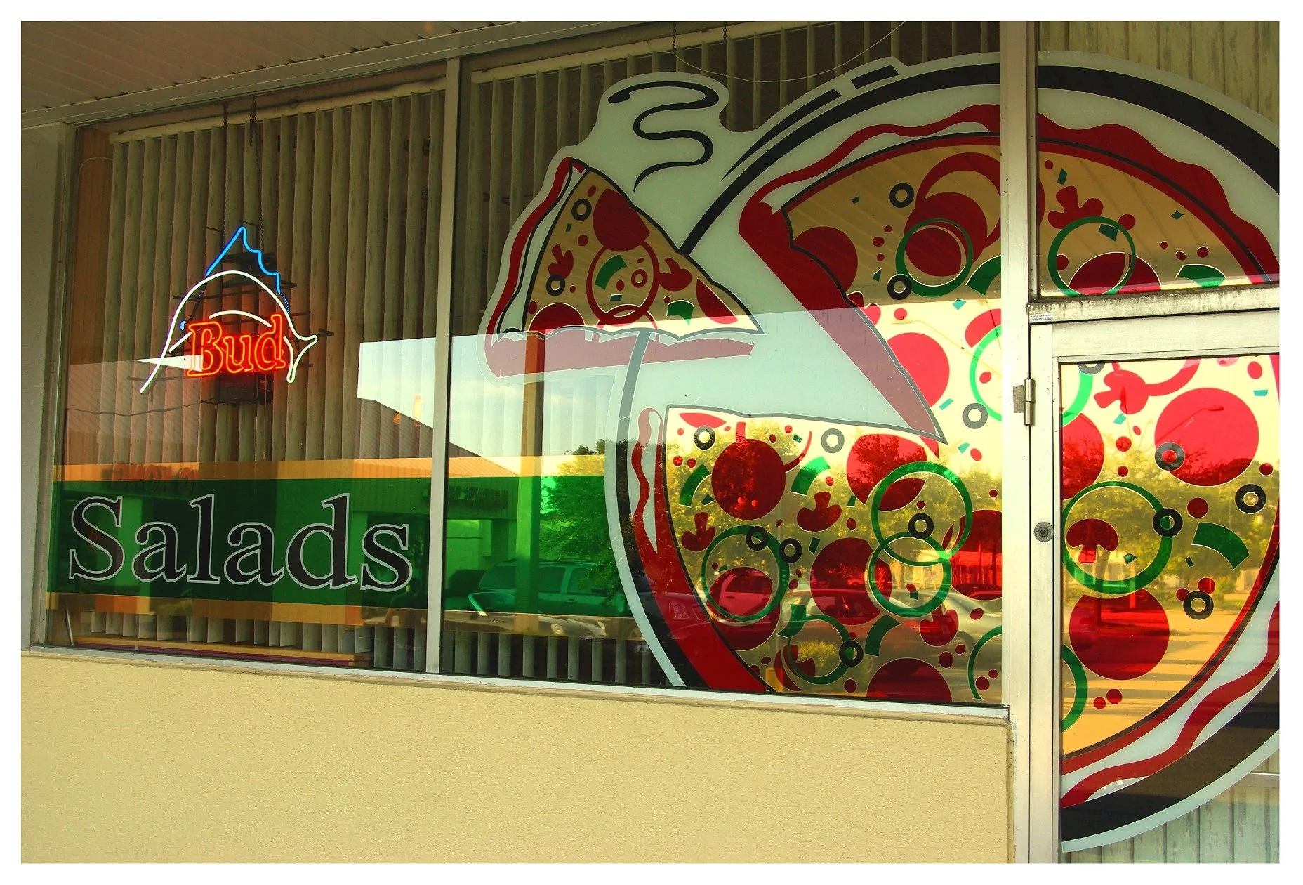 Restaurant window with pizza and salad graphics, and a neon "Bud" sign. colored window film
