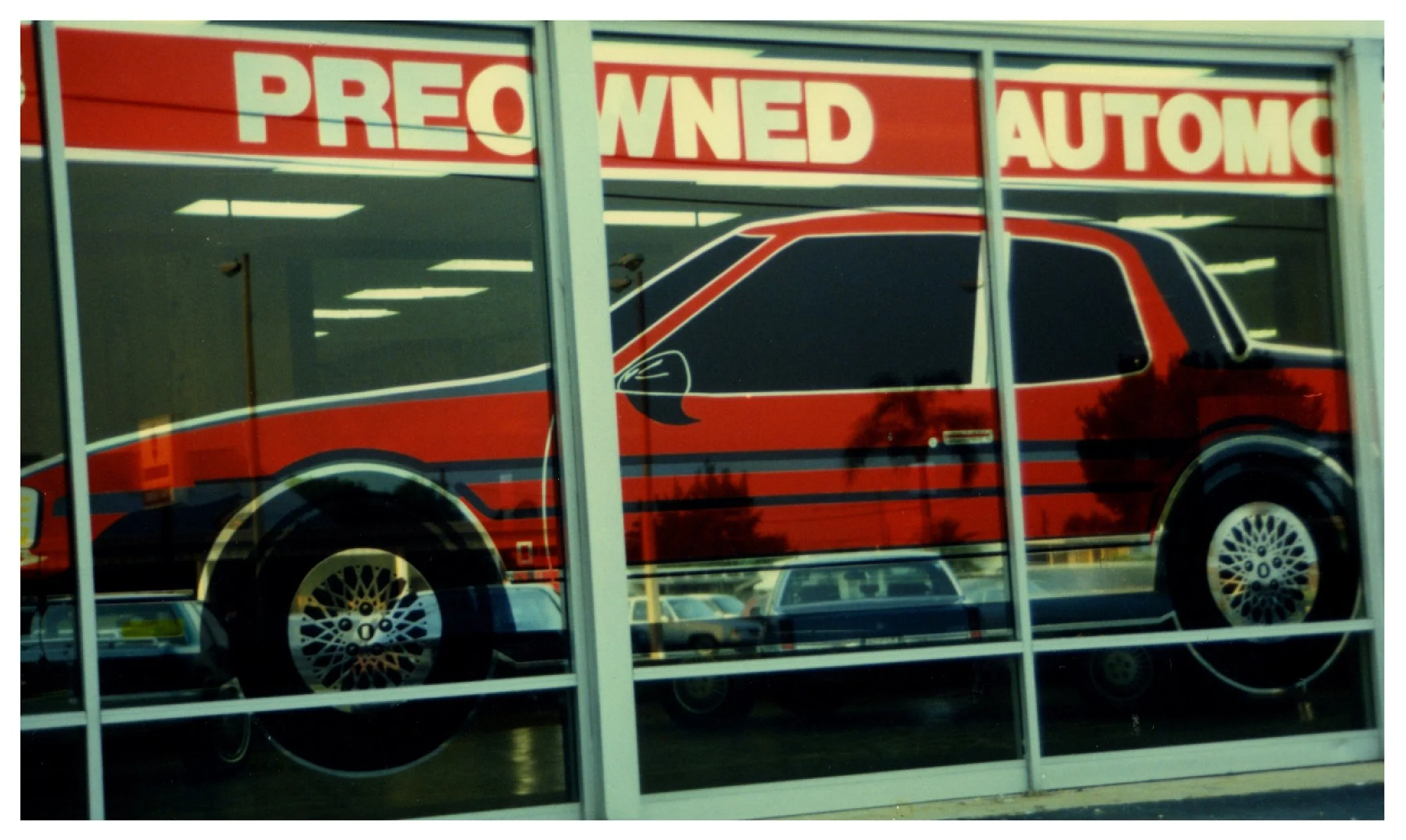 Window display of a pre-owned car dealership with a large red graphic of a luxury sedan on the glass. colored window film colored window film