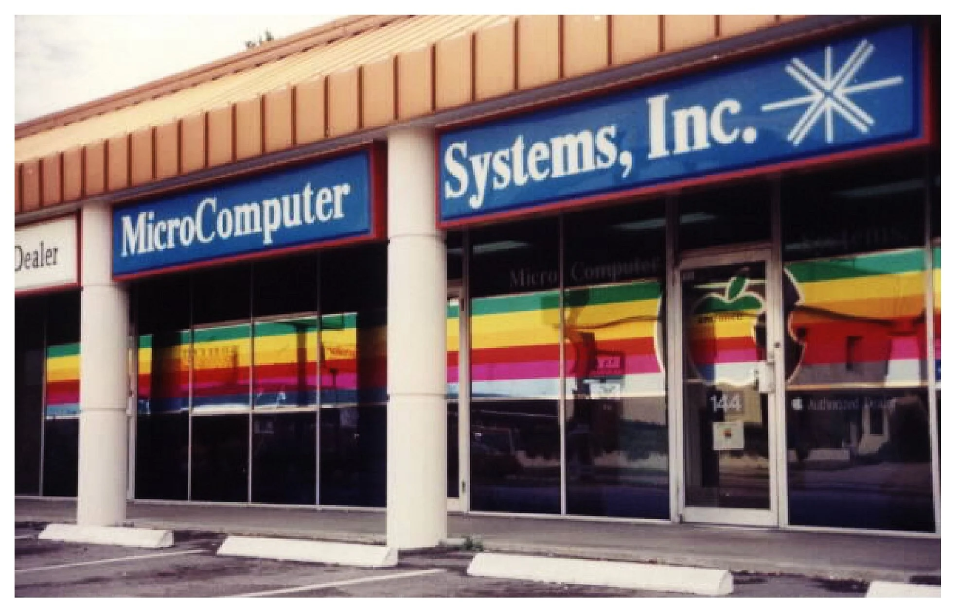 Exterior of a computer store with signage reading "MicroComputer Systems, Inc." and a rainbow-striped window display. colored window film