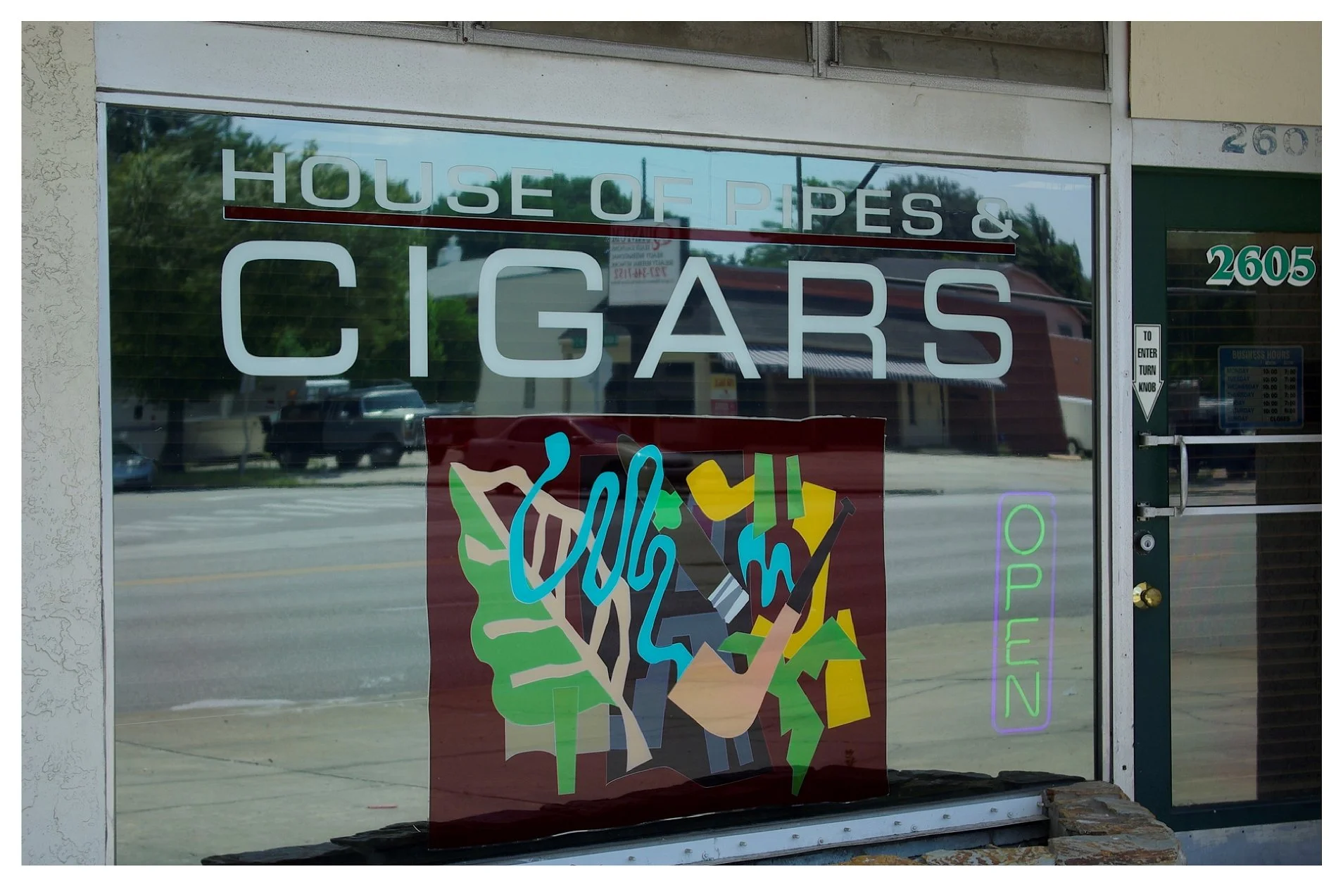 Storefront window displaying "House of Pipes & Cigars" and an "Open" sign with abstract art on the glass. colored window film