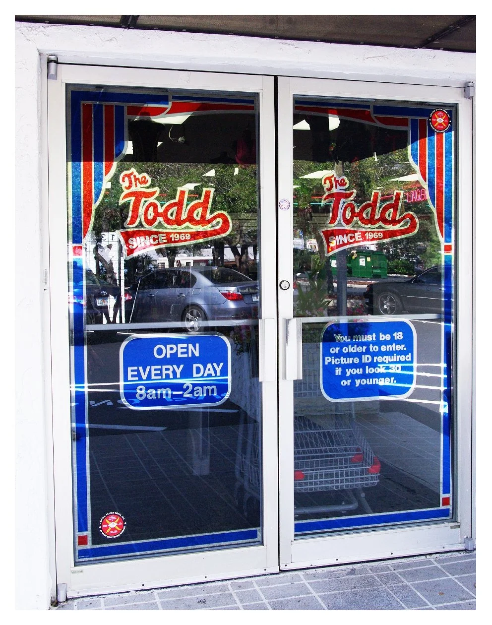 Glass doors of 'The Todd' store, featuring colorful logo and operating hours, open daily from 8am to 2am, with age restriction notice for entry requiring ID. colored window film