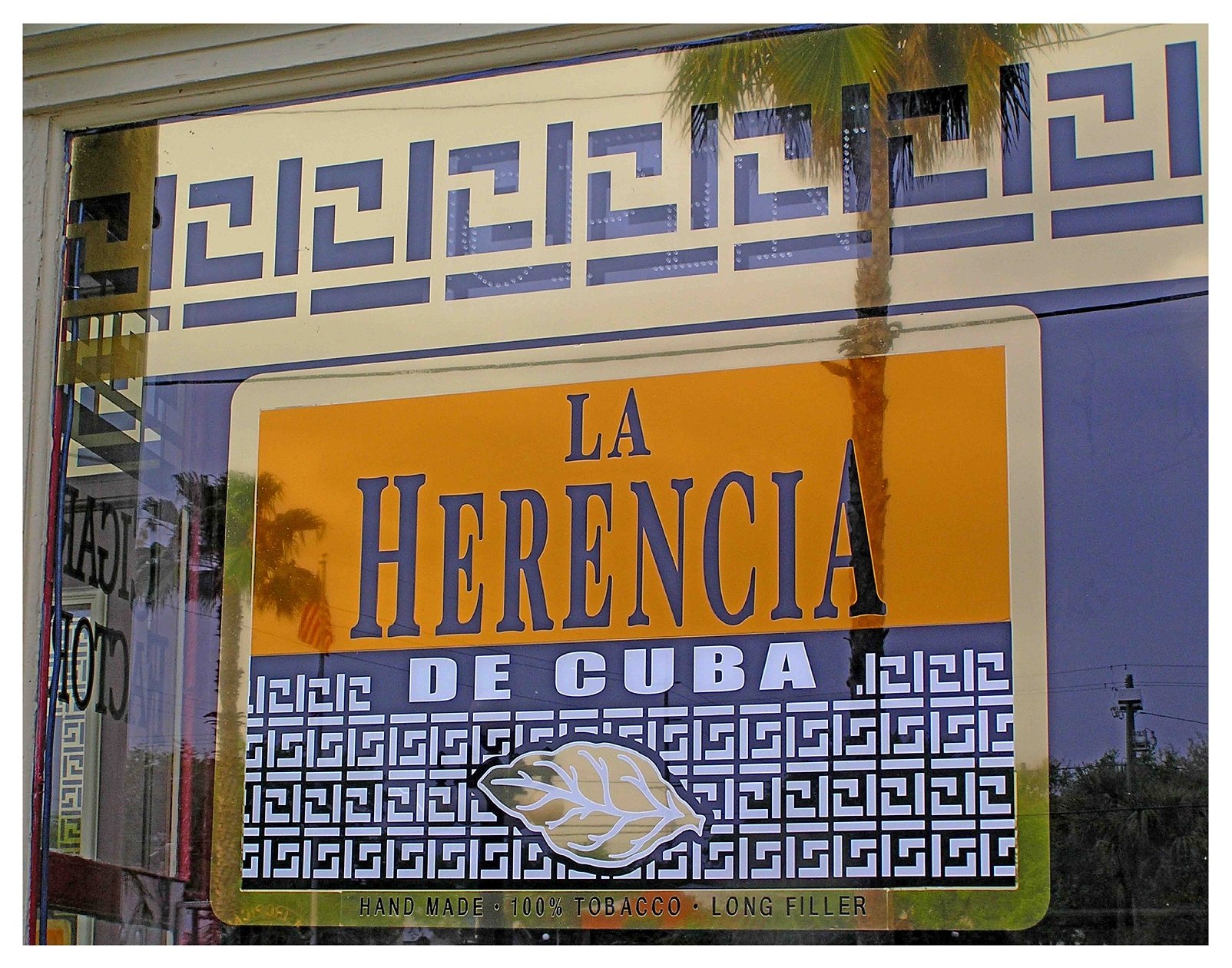 Sign for La Herencia De Cuba with leaf graphic, indicating handmade 100% tobacco, long filler. colored window film