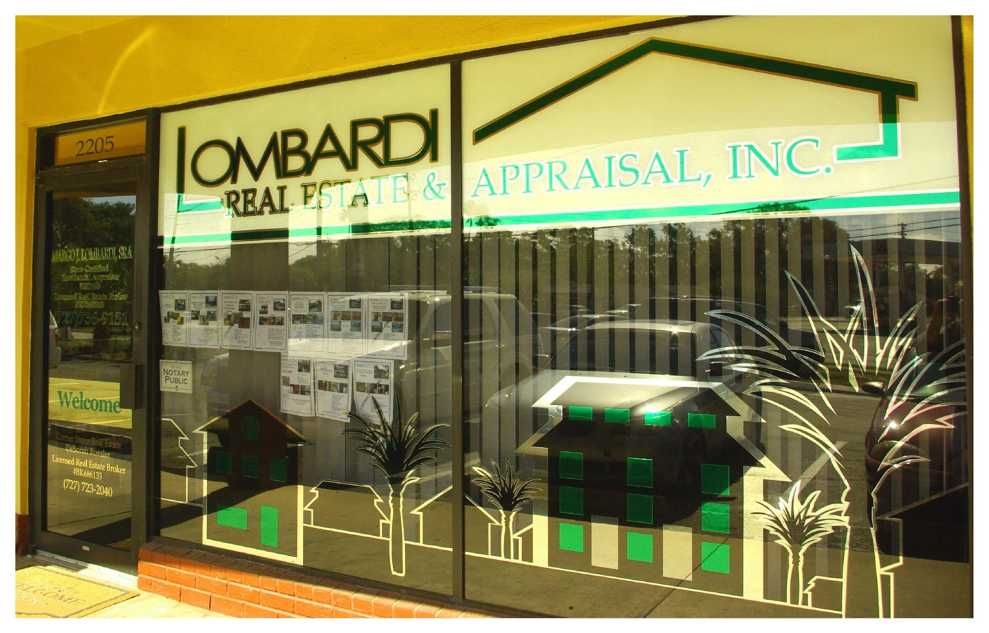 Lombardi Real Estate & Appraisal office front with decorative window graphics, displaying property listings and company signage. colored window film