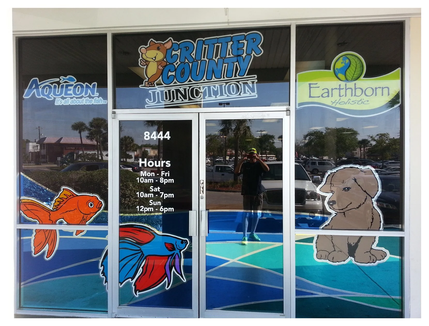 Pet store entrance with signage and images of fish and a dog, Critter County Junction branding, business hours displayed on glass door. colored window film
