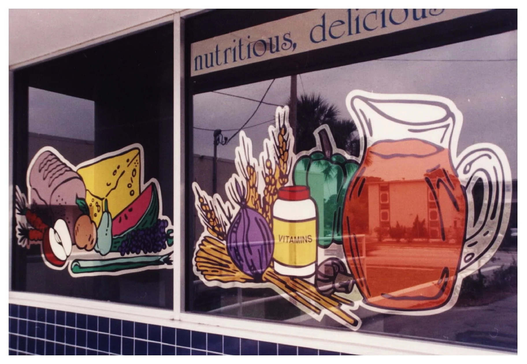 Storefront window with illustrations of food items, including bread, cheese, watermelon, vegetables, vitamin bottle, and a pitcher. The text "nutritious, delicious" is partially visible. colored window film