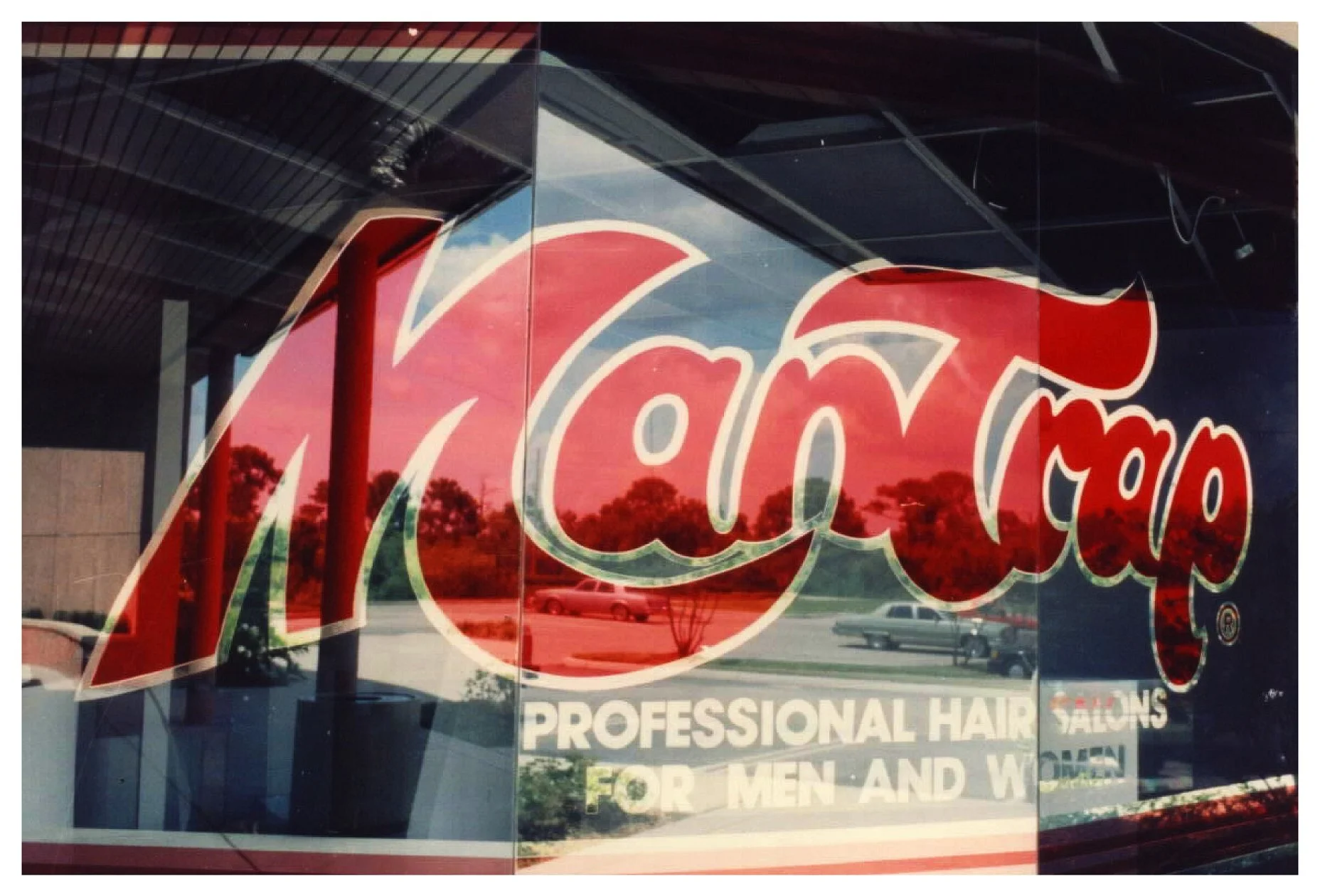 Storefront sign with 'Man Trap' lettering and reflection of surroundings colored window film