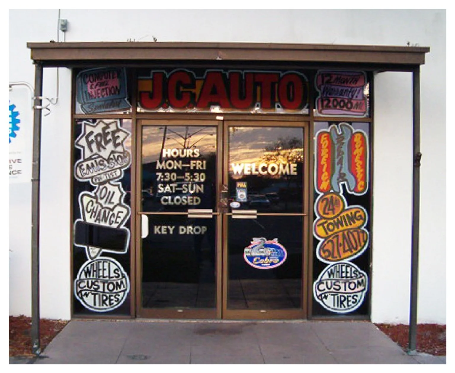 Entrance of JC Auto service shop with promotional signs and business hours. colored window film