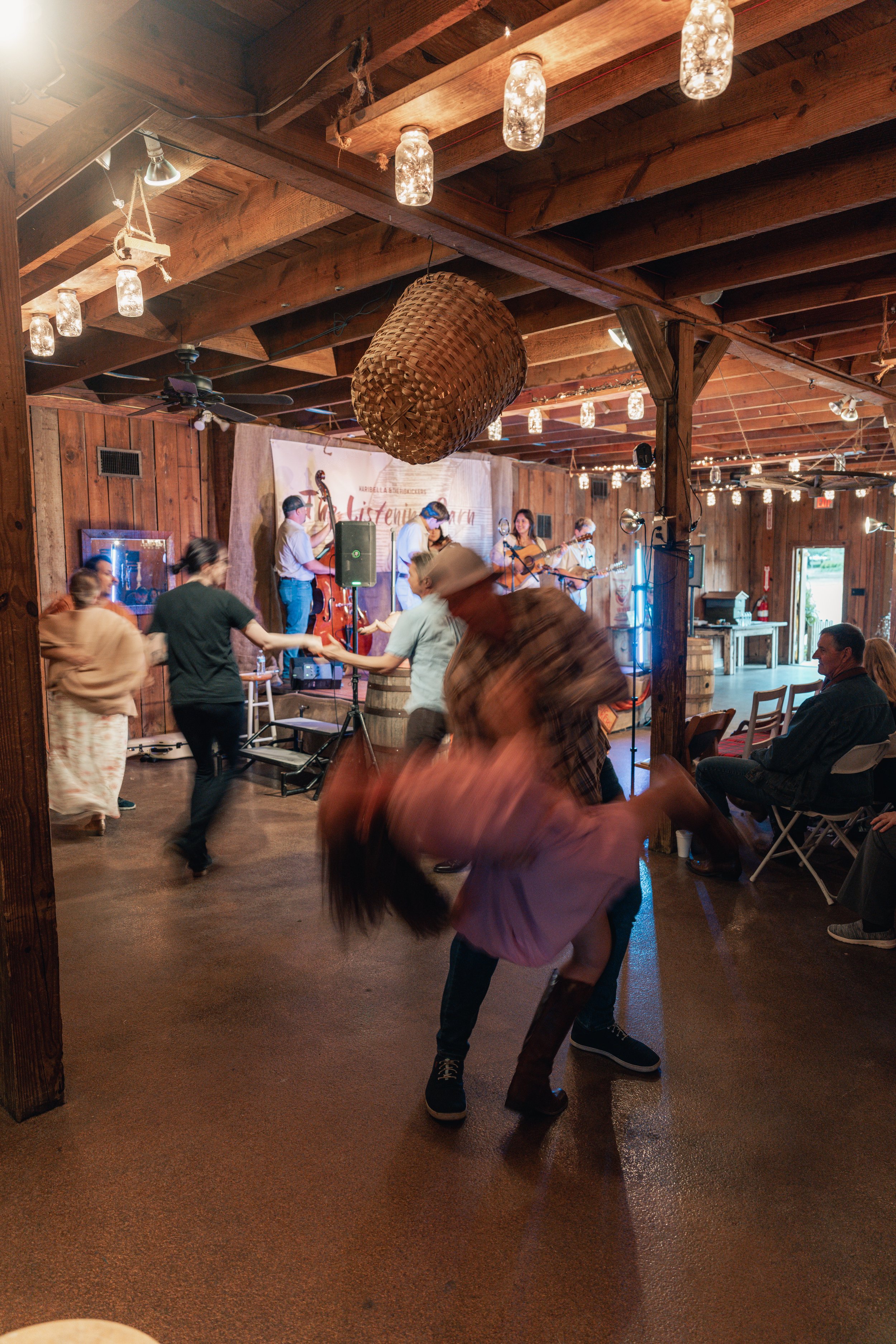 People dancing to a bluegrass band at a rustic barn.