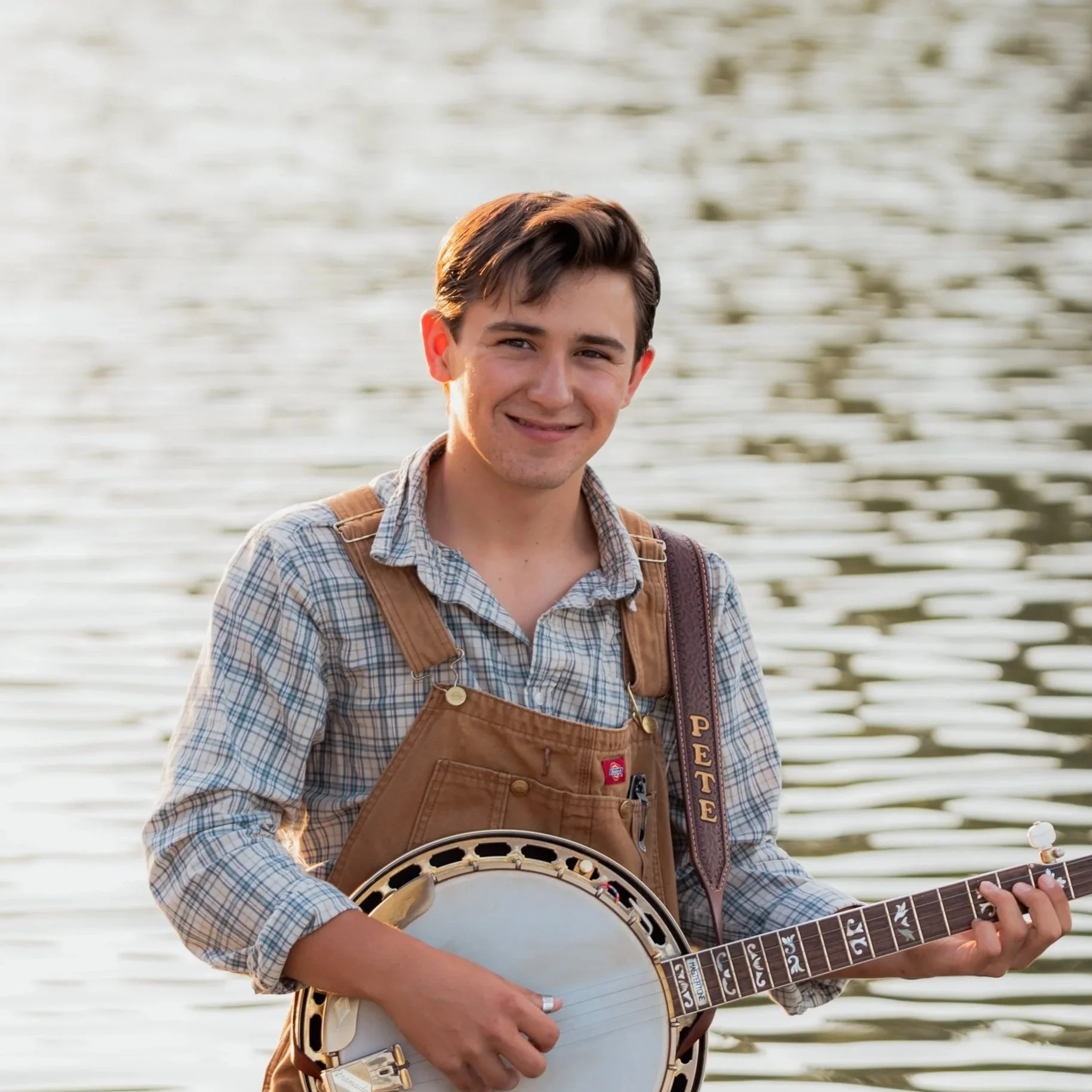 Young boy, Pete, holding a banjo, standing outdoors with a wooden fence in the background, dressed in a blazer and plaid shirt.