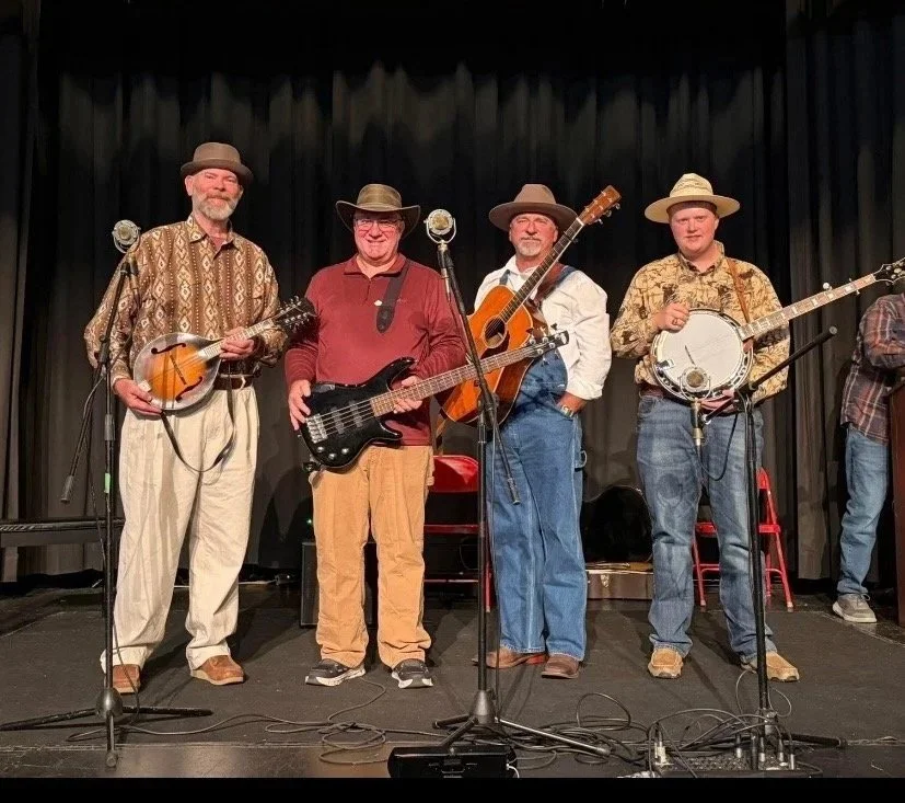 Four men playing string instruments on stage with black curtains in the background.