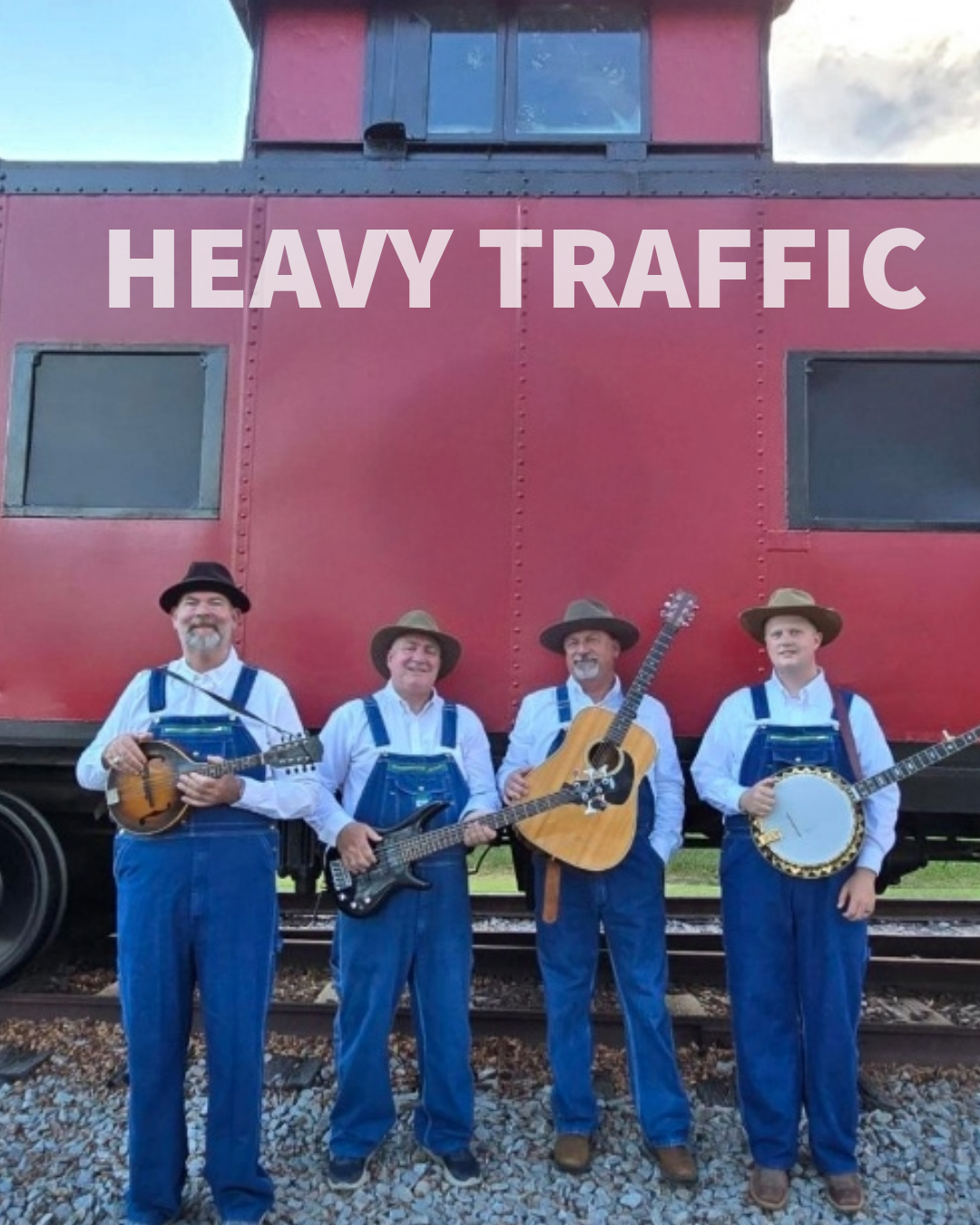 Four men dressed in overalls and hats standing in front of a red train car, holding musical instruments. The front of the train car has the words 'HEAVY TRAFFIC' written on it.