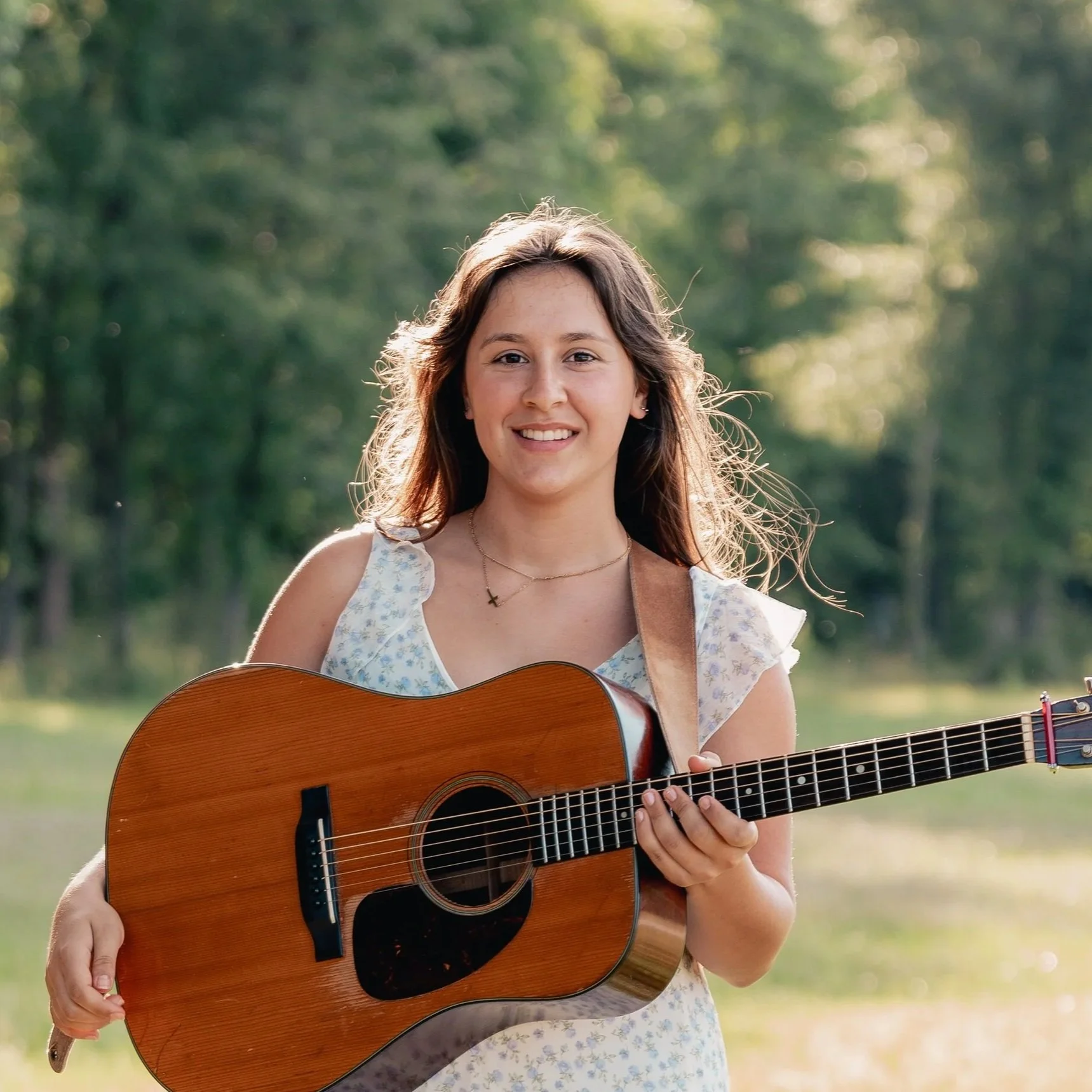 Young woman, AnnMari, wearing a white cowboy hat, sitting outdoors and holding an acoustic guitar.