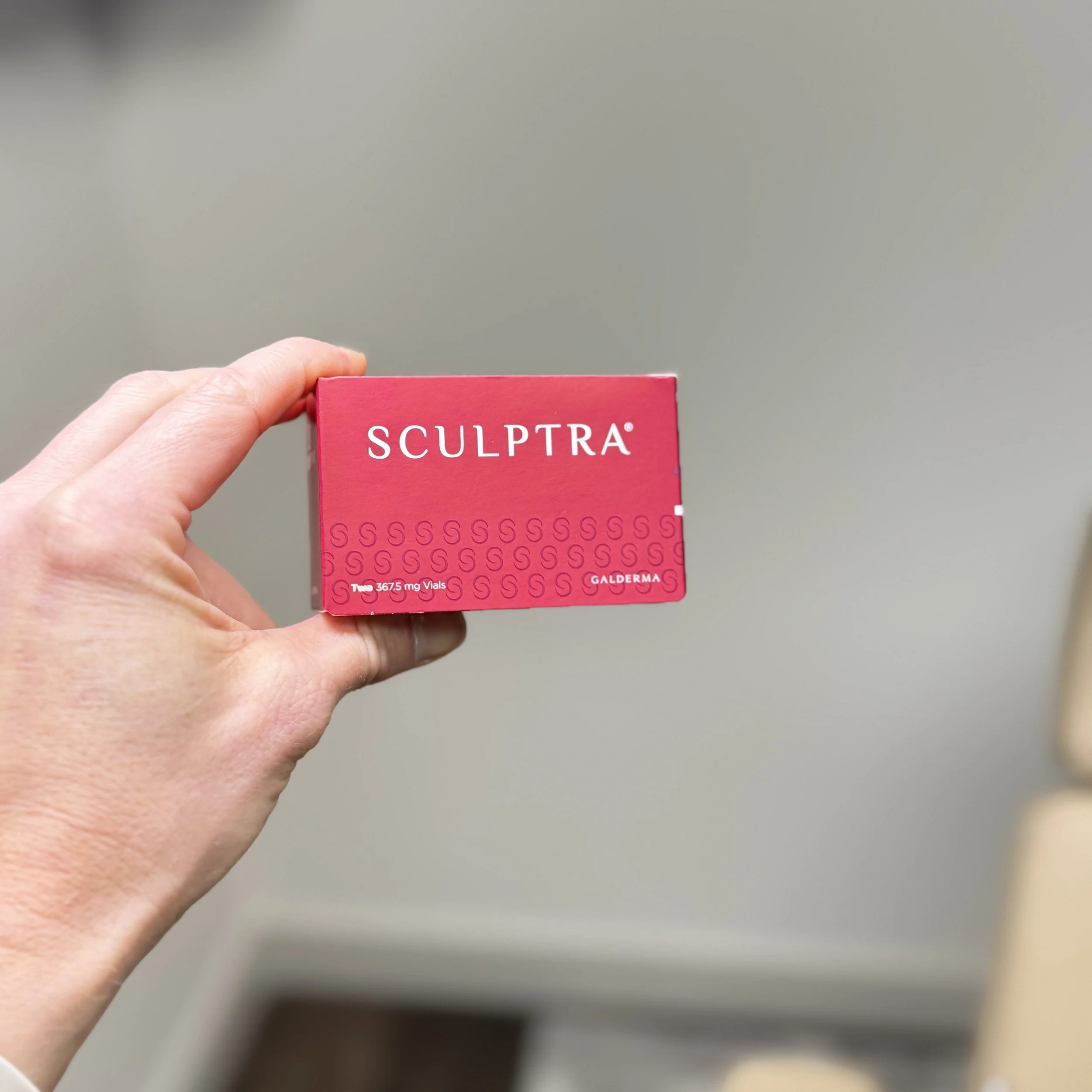 A person's hand holding a pink box labeled 'Sculptra'