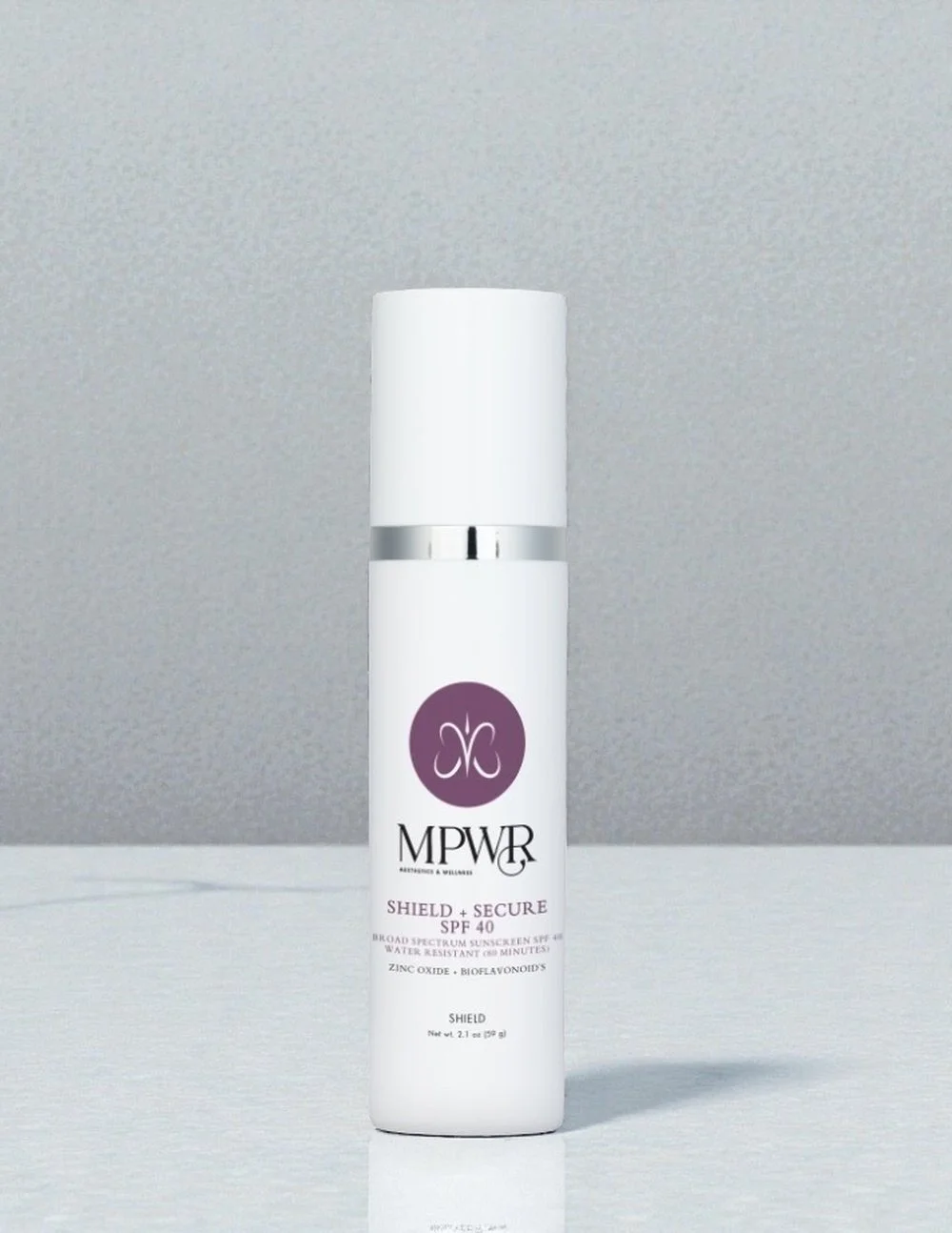 A silver and white bottle of MPWR Shield + Secure SPF 40 broad spectrum sunscreen with a pump dispenser and transparent cap.