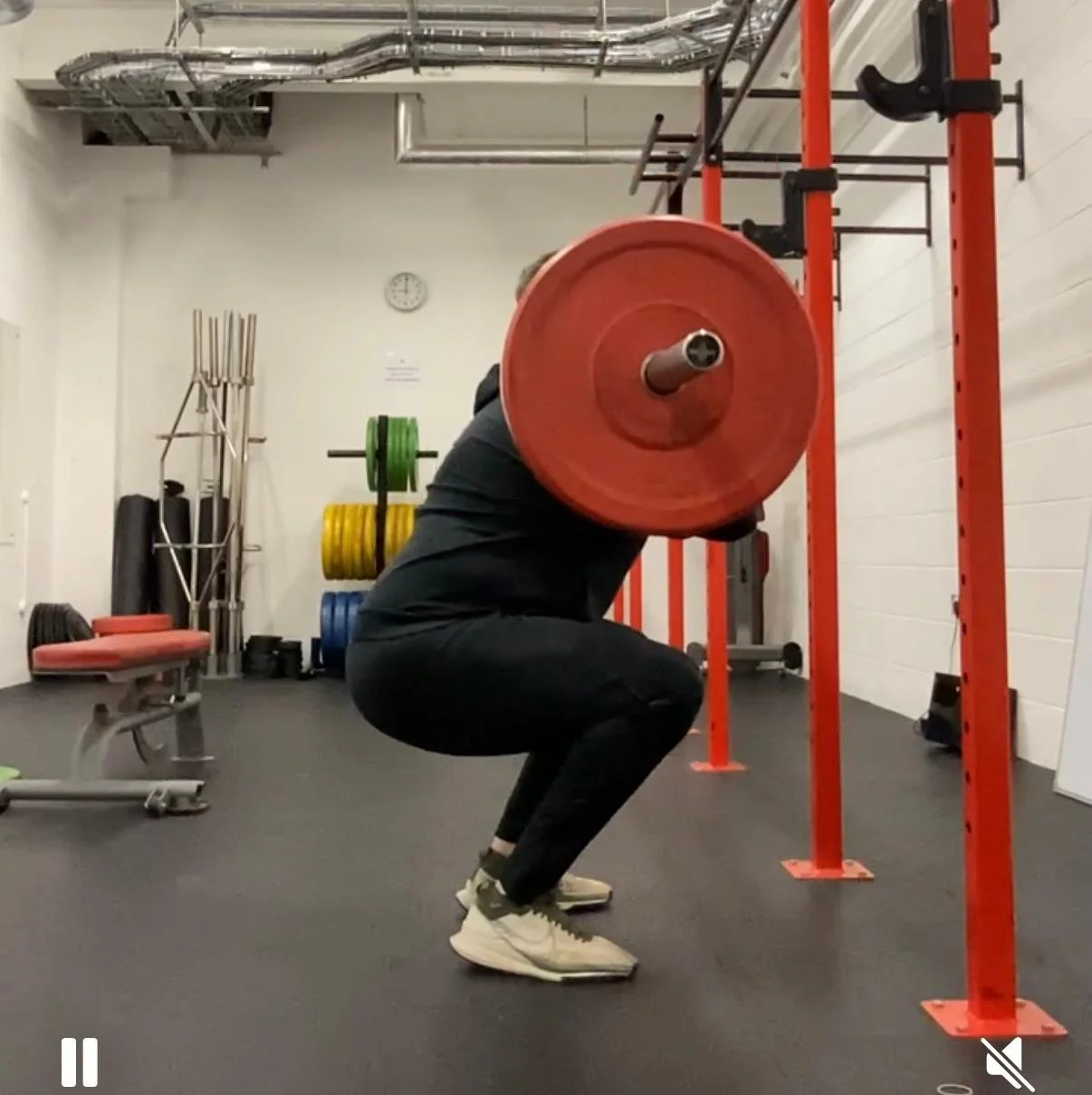 Person performing a squat exercise with a barbell loaded with red weight plates in a gym.