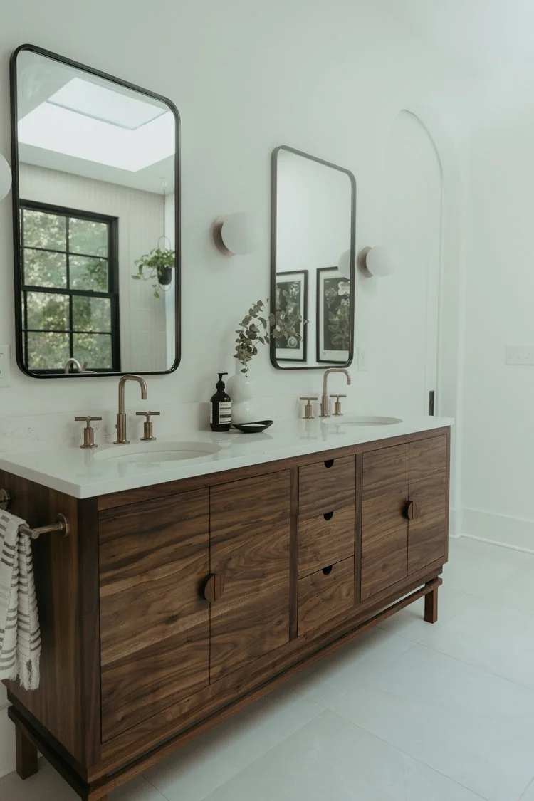 Modern bathroom with wooden vanity, two sinks, large mirrors, and wall sconces.