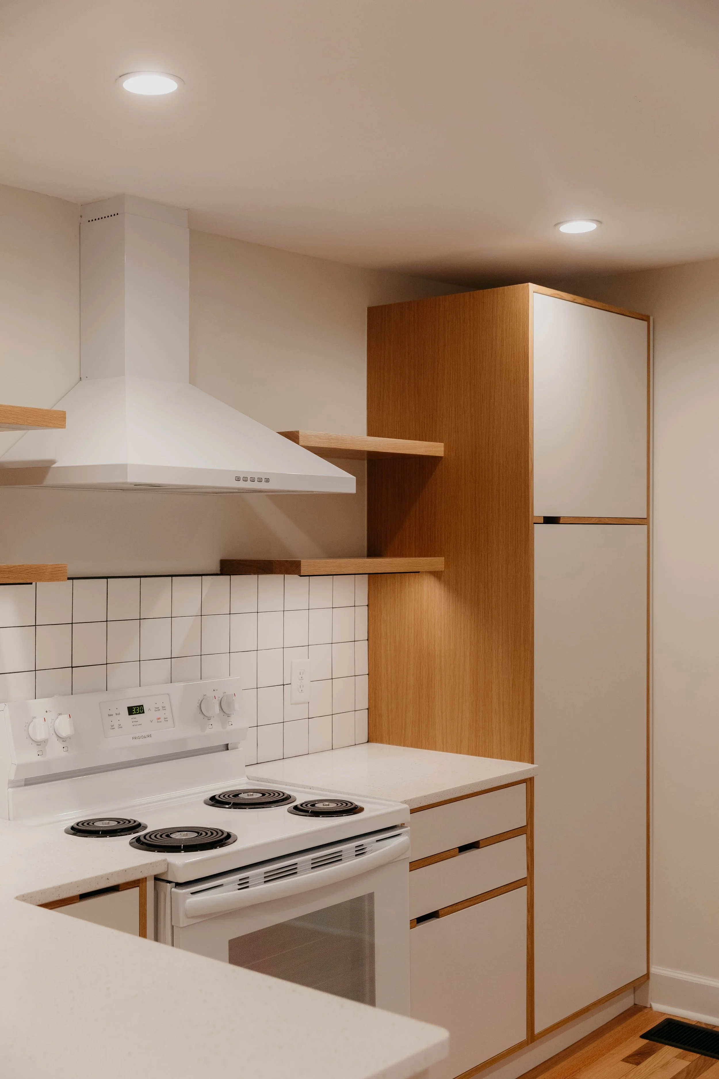 Modern kitchen with white electric stove, tile backsplash, wooden cabinets, floating shelves, and white range hood.