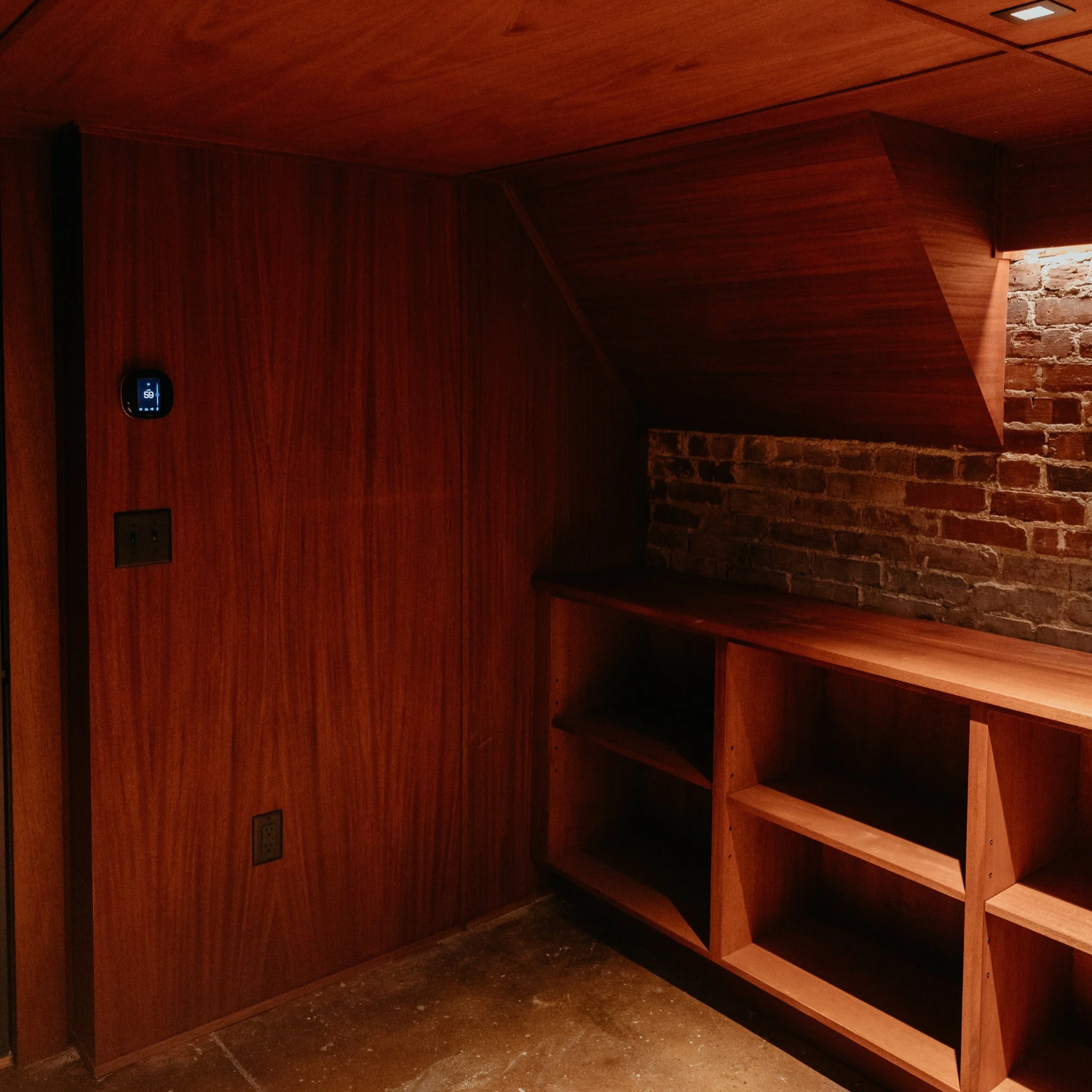 Wood-paneled room with brick accent wall, wooden shelving, and a digital thermostat on the wall.
