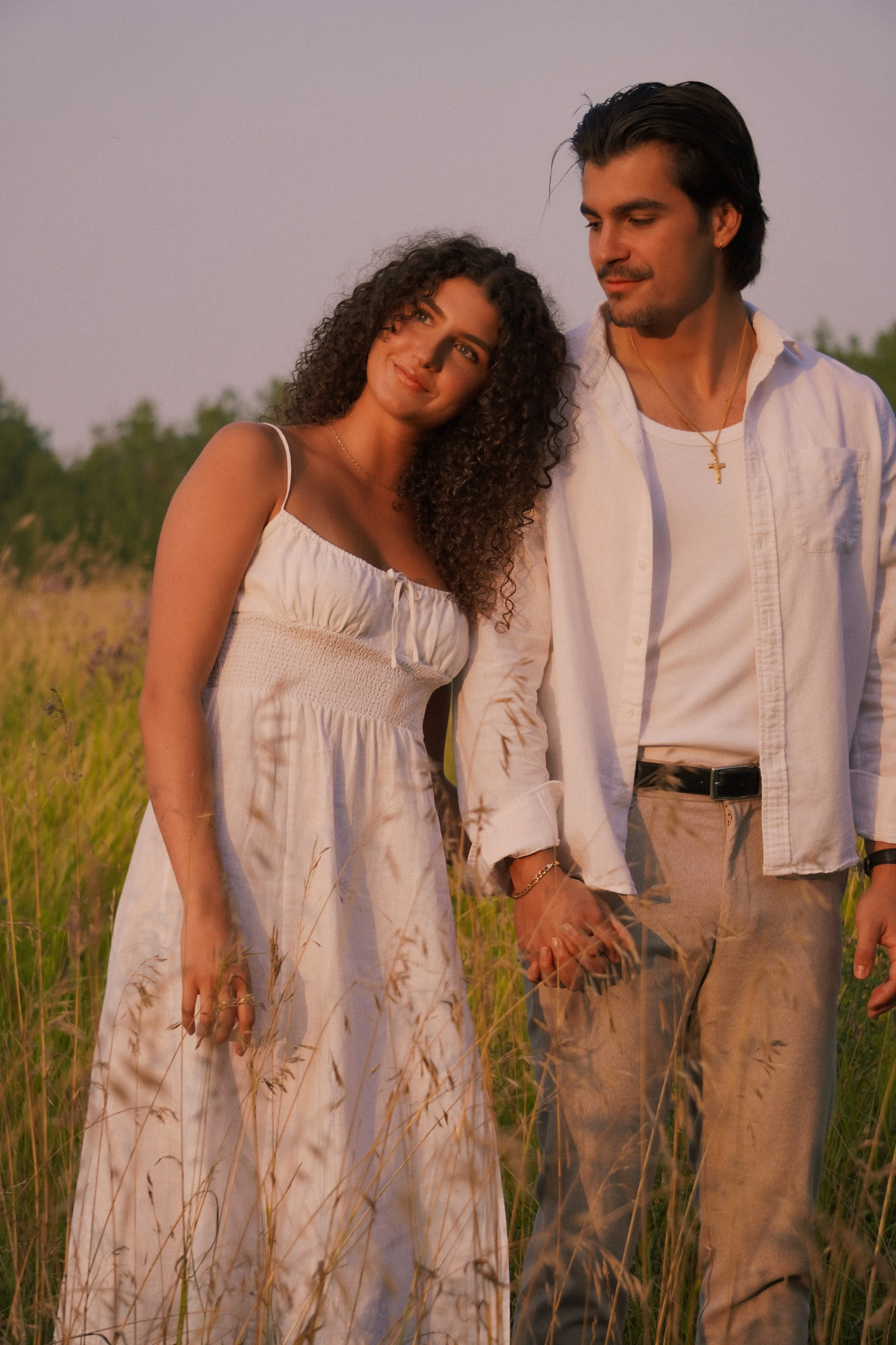 Engagement photoshoot in Edmonton — young couple holding hands in grassy field during golden hour.