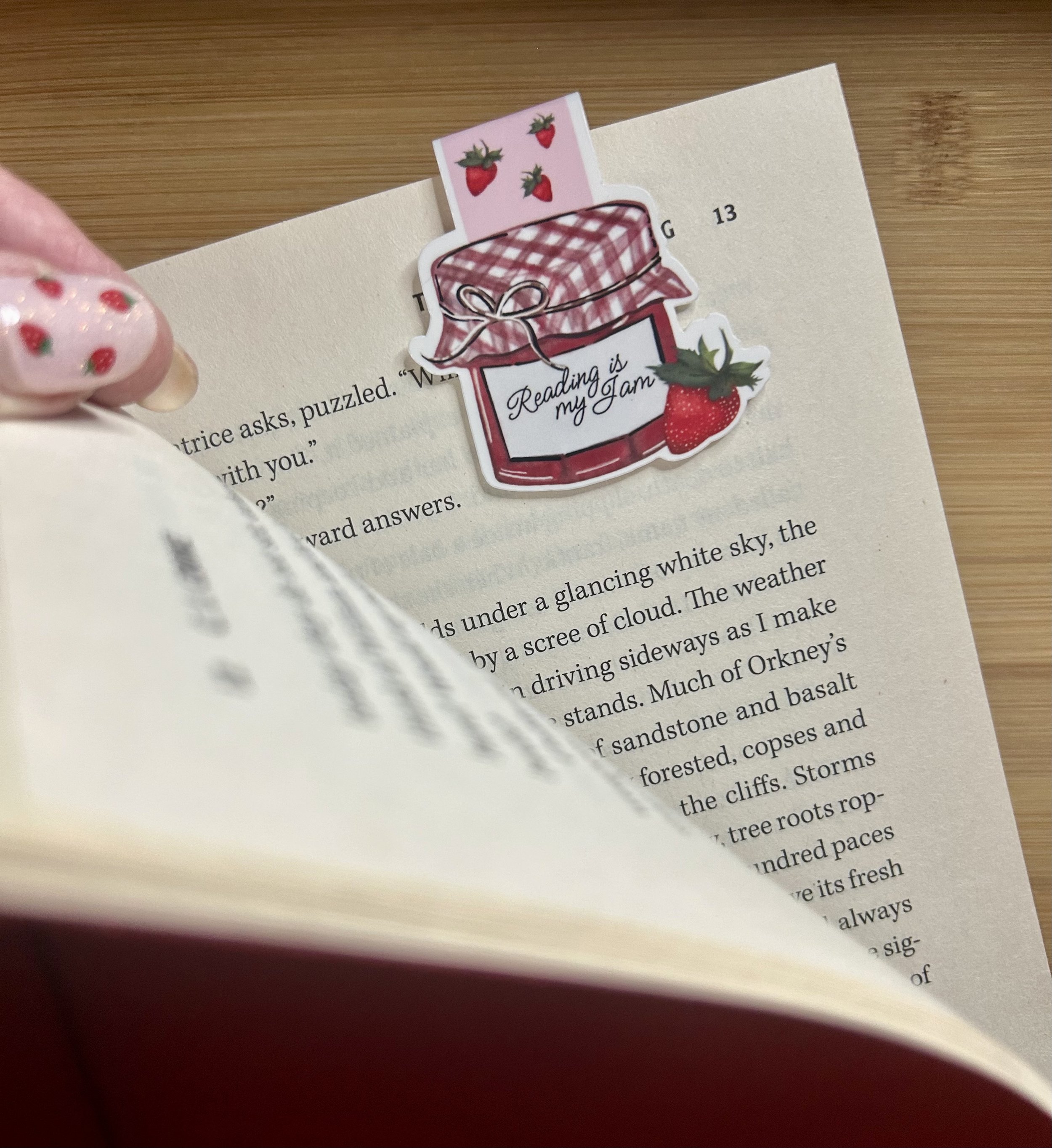 Handcrafted Reading Is My Jam strawberry magnetic bookmark holding a page in an open book from the Gather Strawberry Summer Collection shown in place on book.