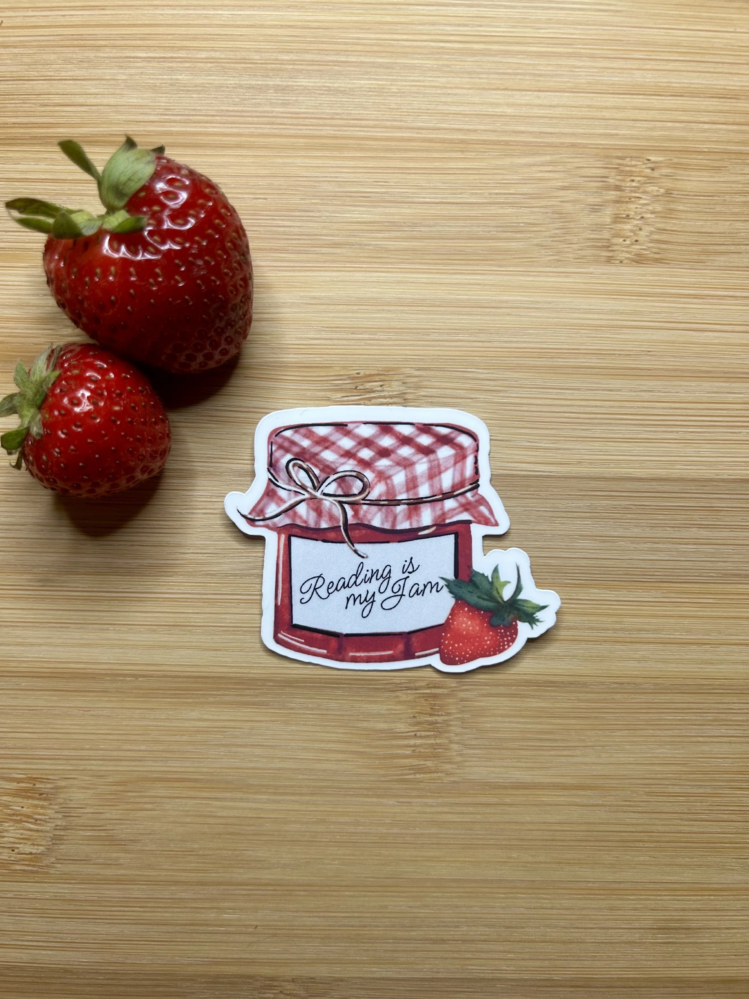 Hand-illustrated Reading Is My Jam strawberry preserves jar die-cut sticker with pink gingham lid and ripe strawberry.