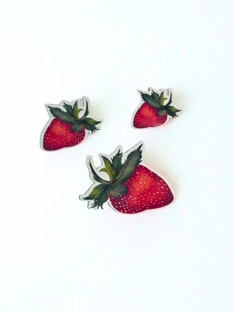 Various sizes of hand-illustrated ripe red strawberry die-cut sticker with leafy green top displayed on a white background.