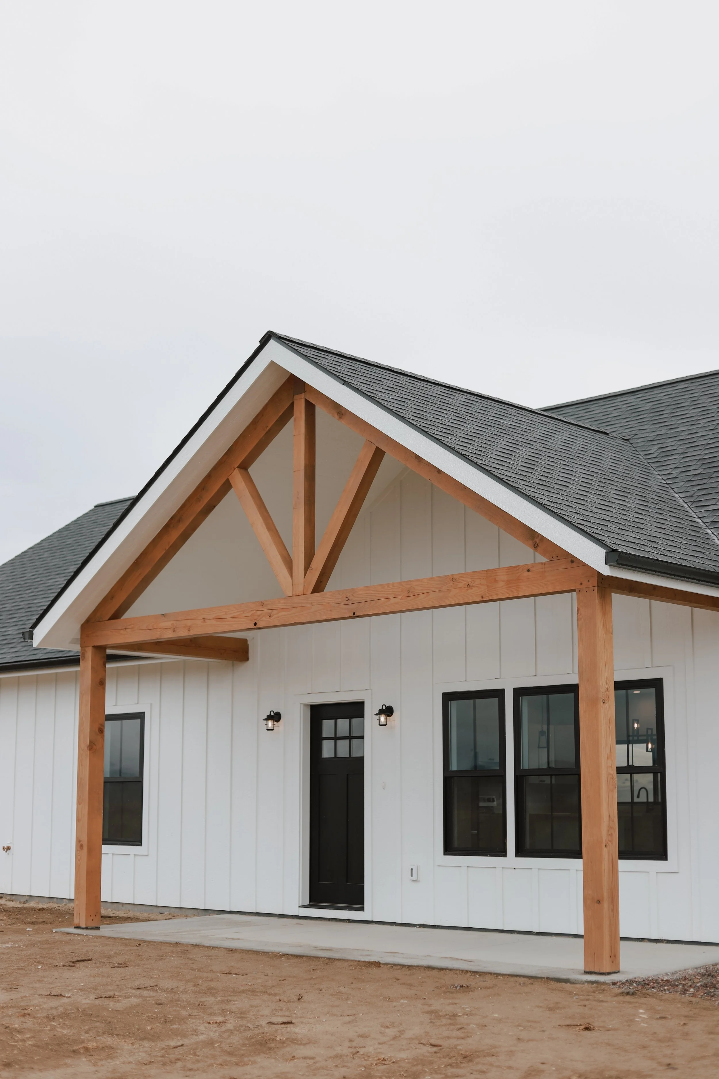 This photo shows a newly built modern-farmhouse in Lonepine, MT by Felts Construction, featuring a timbe-frame gable, natural wood posts, and clean white siding with black-framed windows.