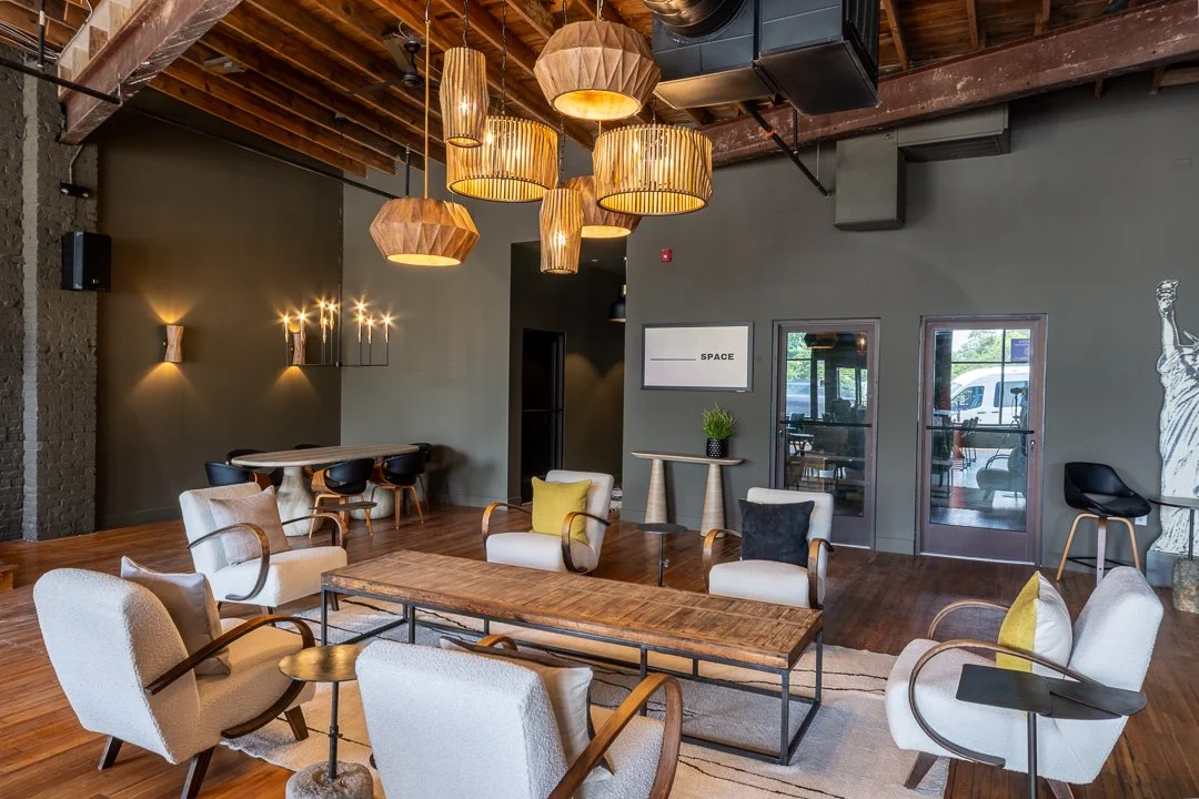 Blank Space favorite event venue Asheville. Modern interior with wooden ceiling, hanging pendant lights, and a mix of white and beige chairs around a wooden coffee table in a lounge or meeting space.