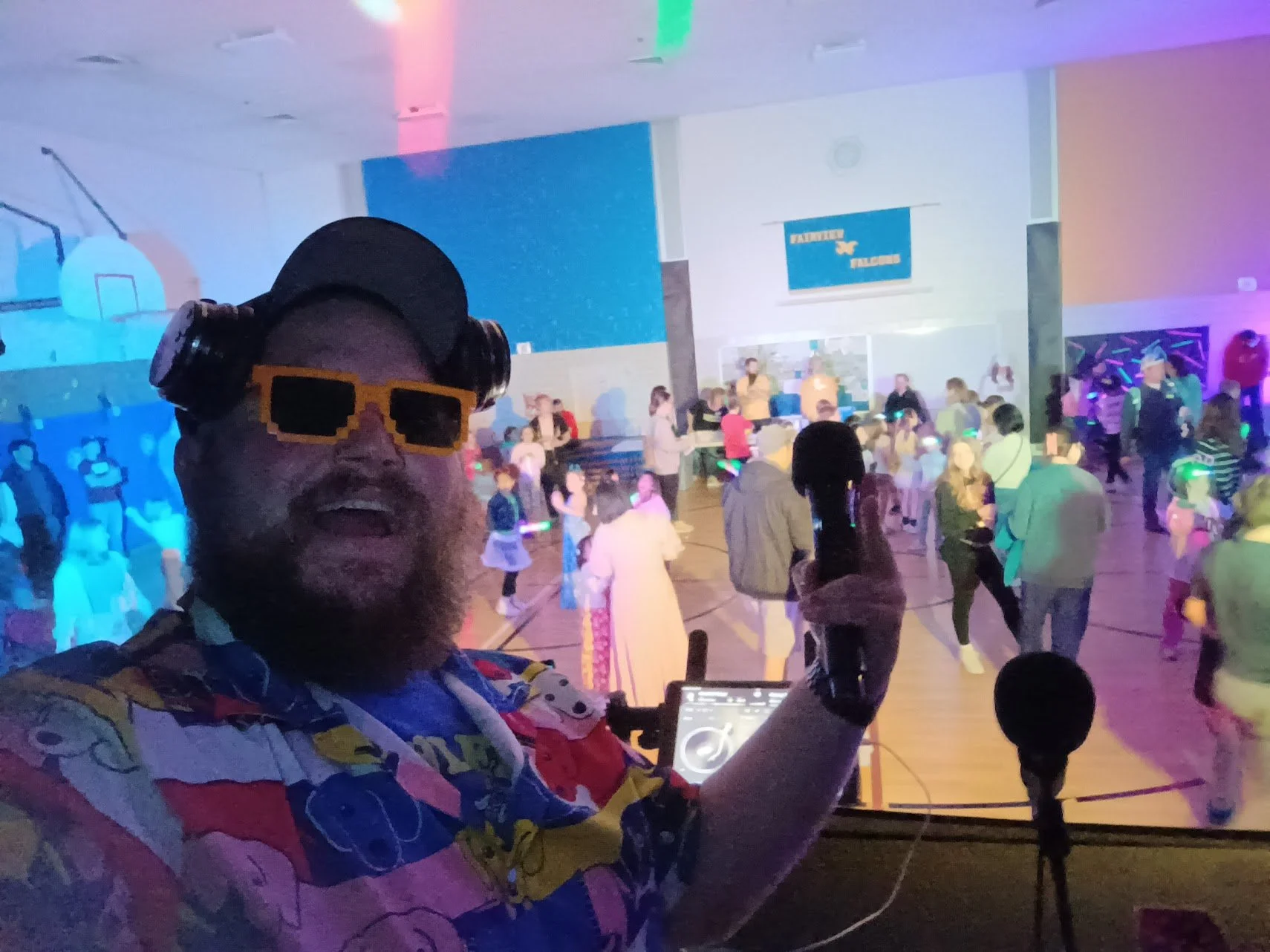 “DJ Jazzy Josh selfie with colorful lighting at a school dance.”