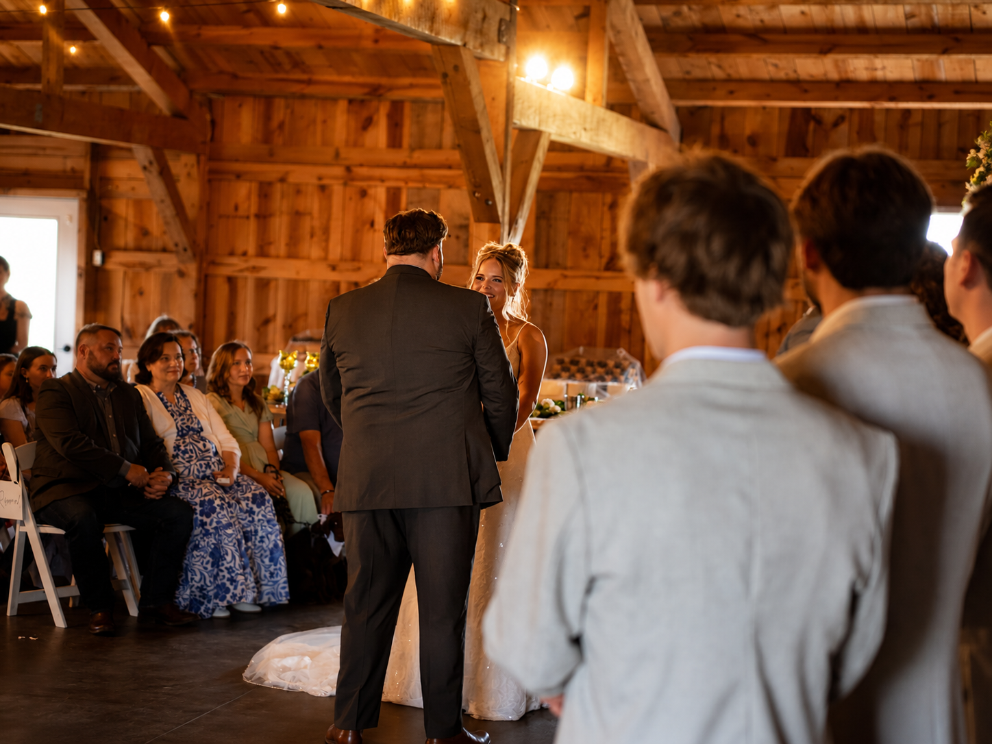 A couple is getting married inside a rustic wooden barn, with guests seated and watching their ceremony.