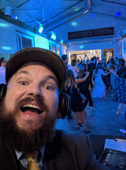 DJ Jazzy Josh entertaining a packed wedding reception with guests dancing under blue party lighting and high-energy music.
