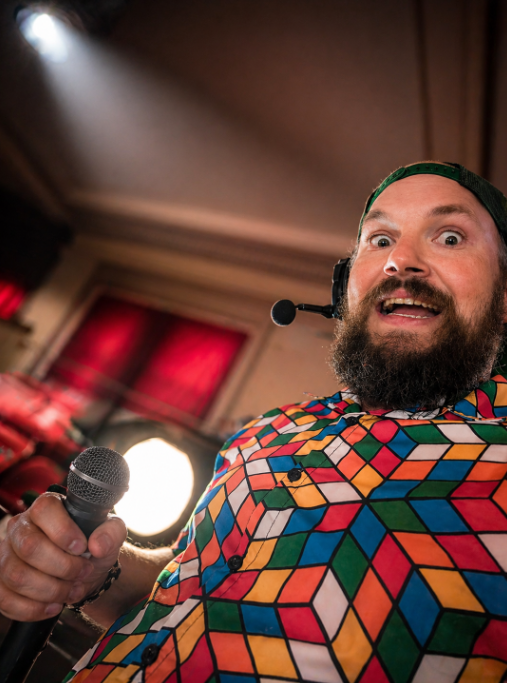 DJ Jazzy Josh wearing colorful retro party attire and headset microphone while entertaining guests with interactive event hosting and party lighting.