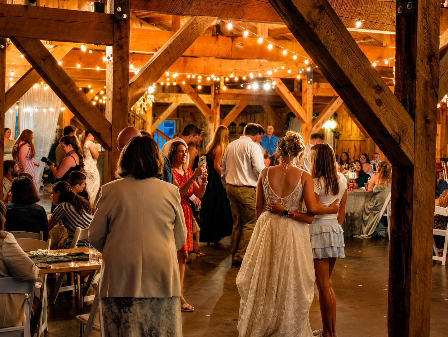 Guests dancing and socializing at a rustic wooden barn wedding reception decorated with string lights.