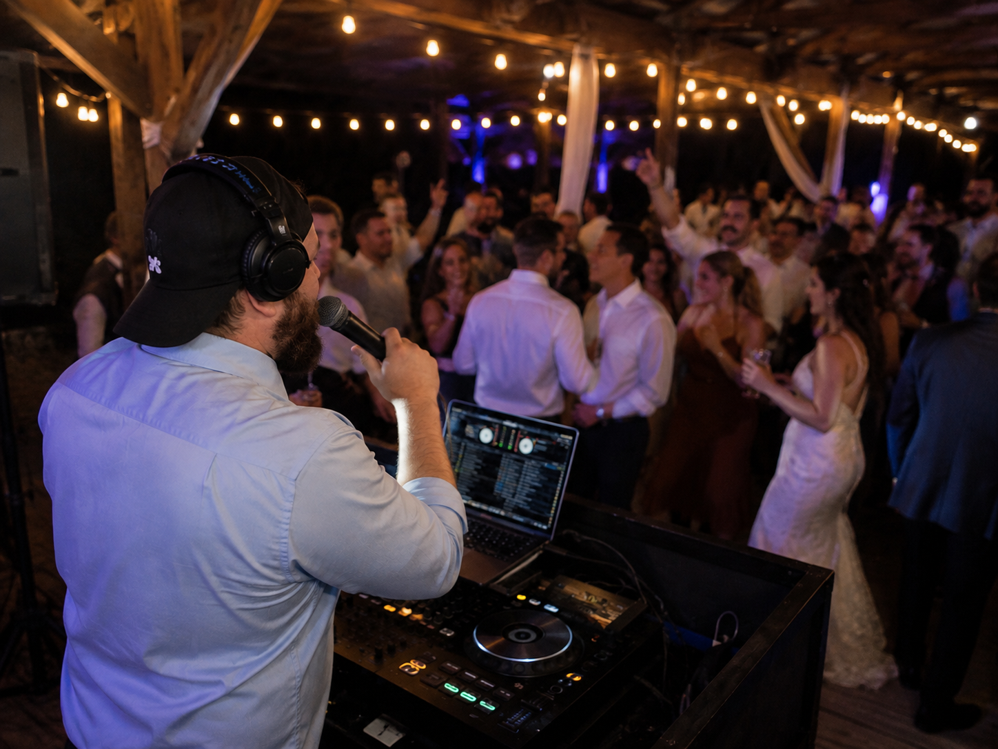 Wedding reception with a DJ playing music, and guests dancing under string lights.