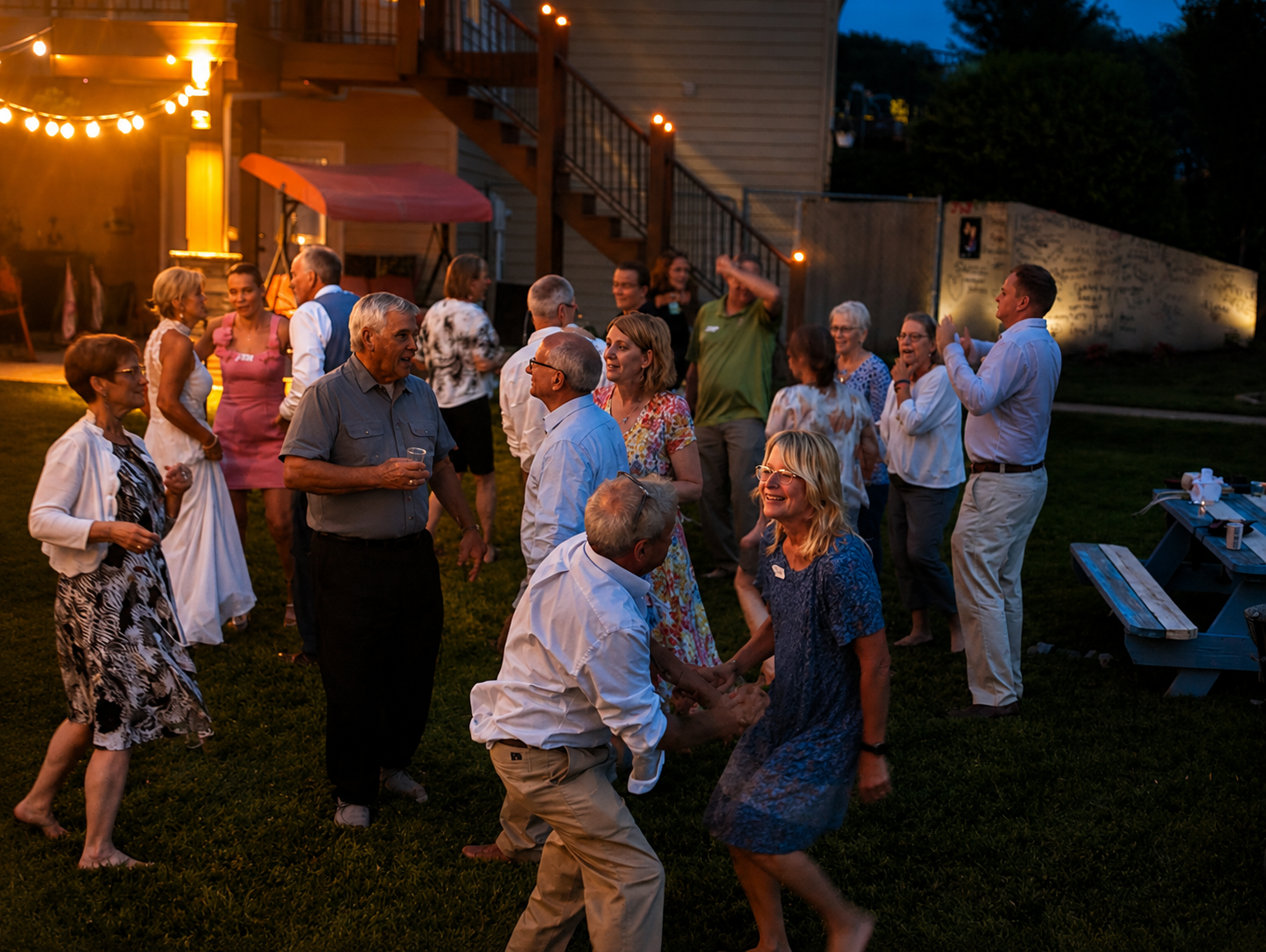 People dancing and socializing at an outdoor evening party with string lights, in a backyard setting.