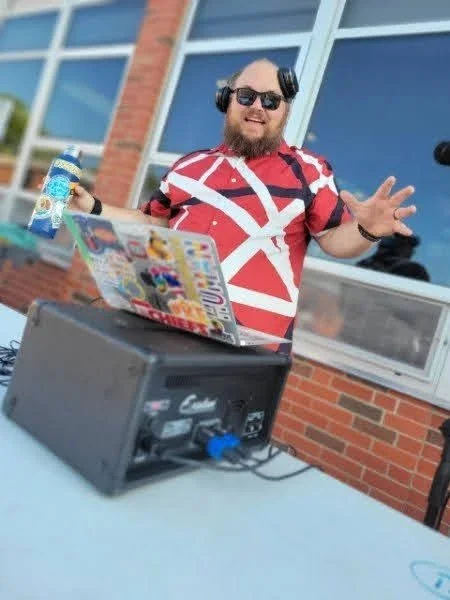 “DJ Jazzy Josh performing at an outdoor college event with branded DJ booth.”