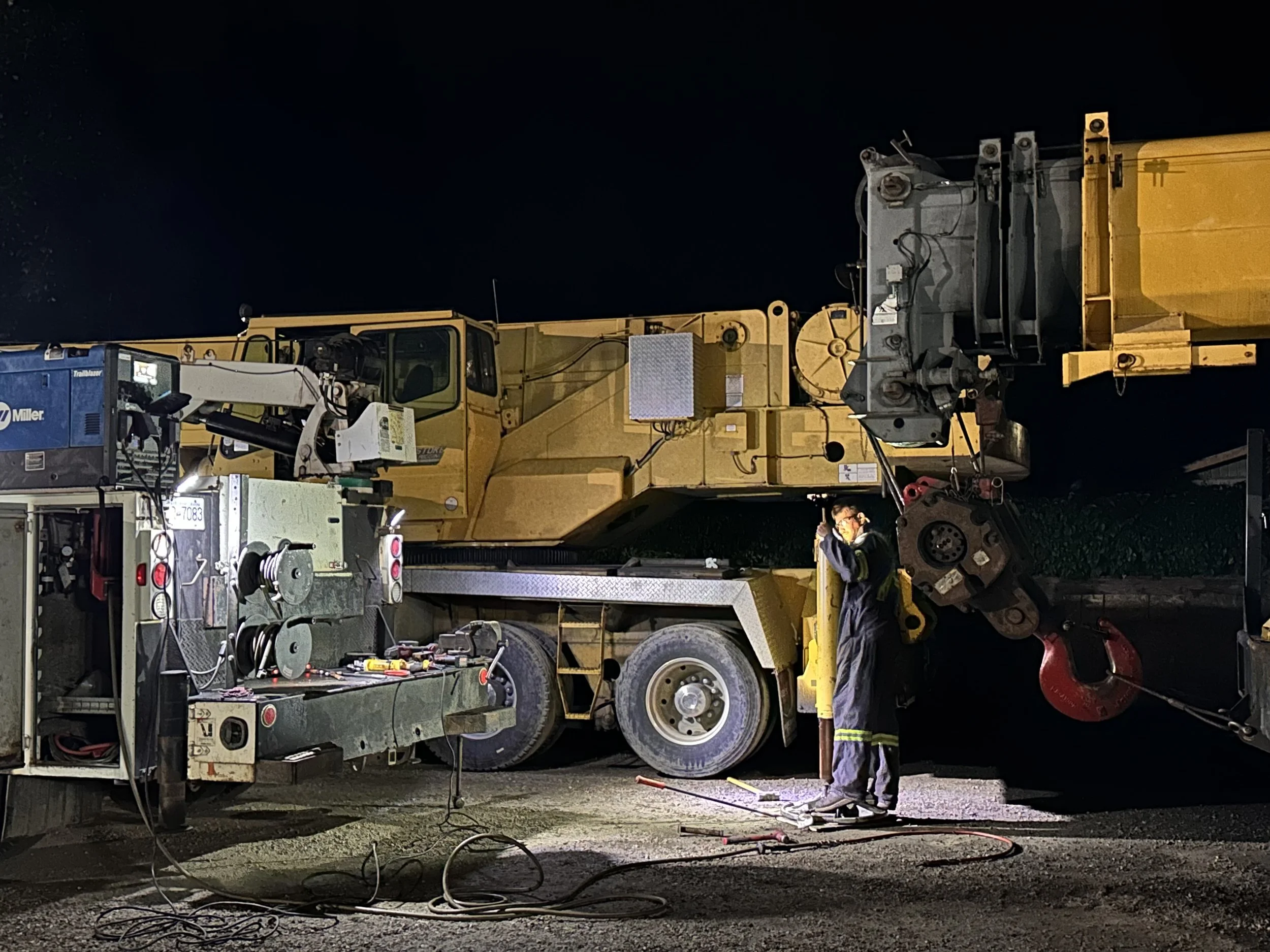 A worker in safety gear operating heavy machinery at night, with tools and equipment around.