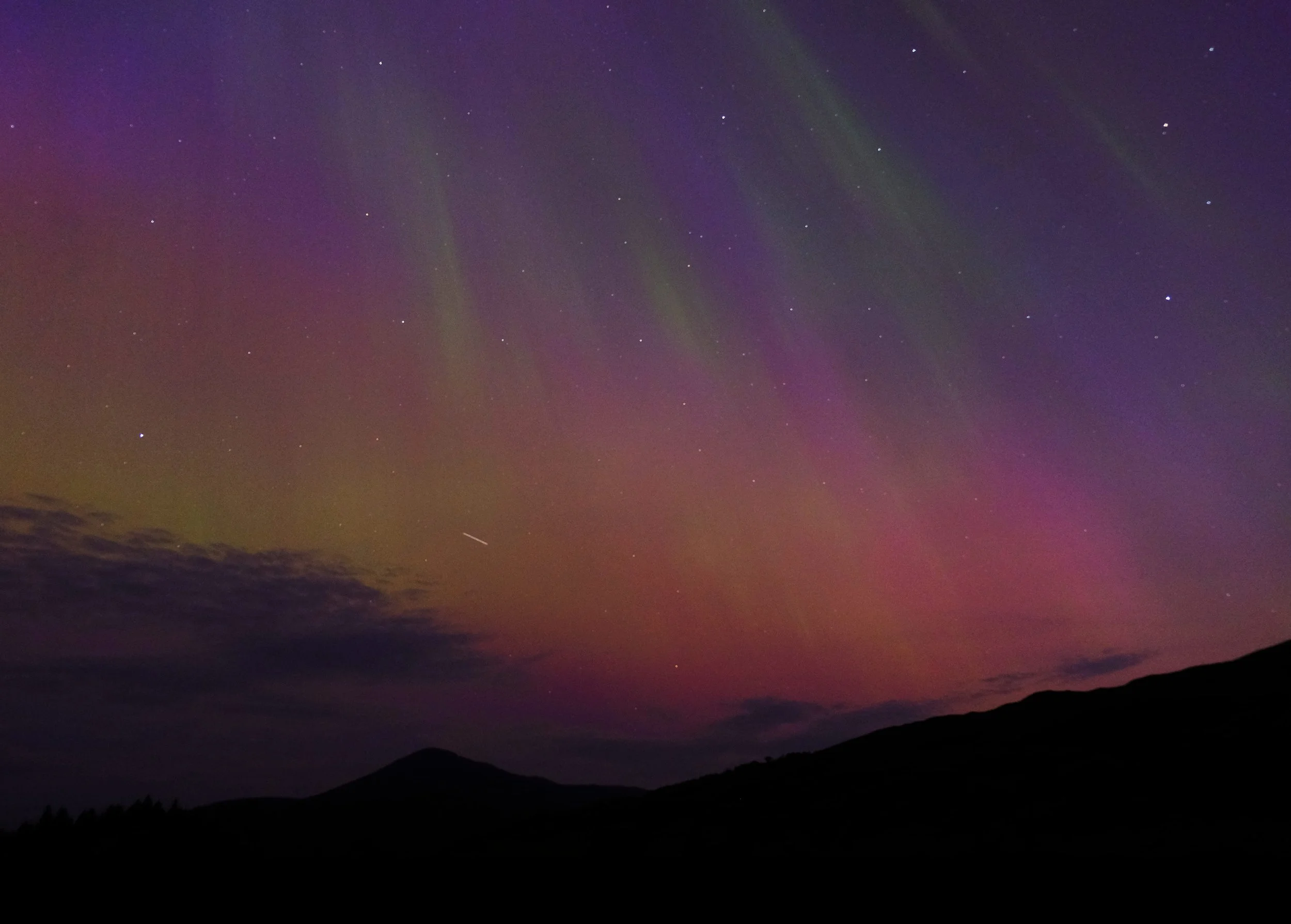 Nordlichter leuchten am Himmel über Bergen bei Nacht, mit Sternen sichtbar.