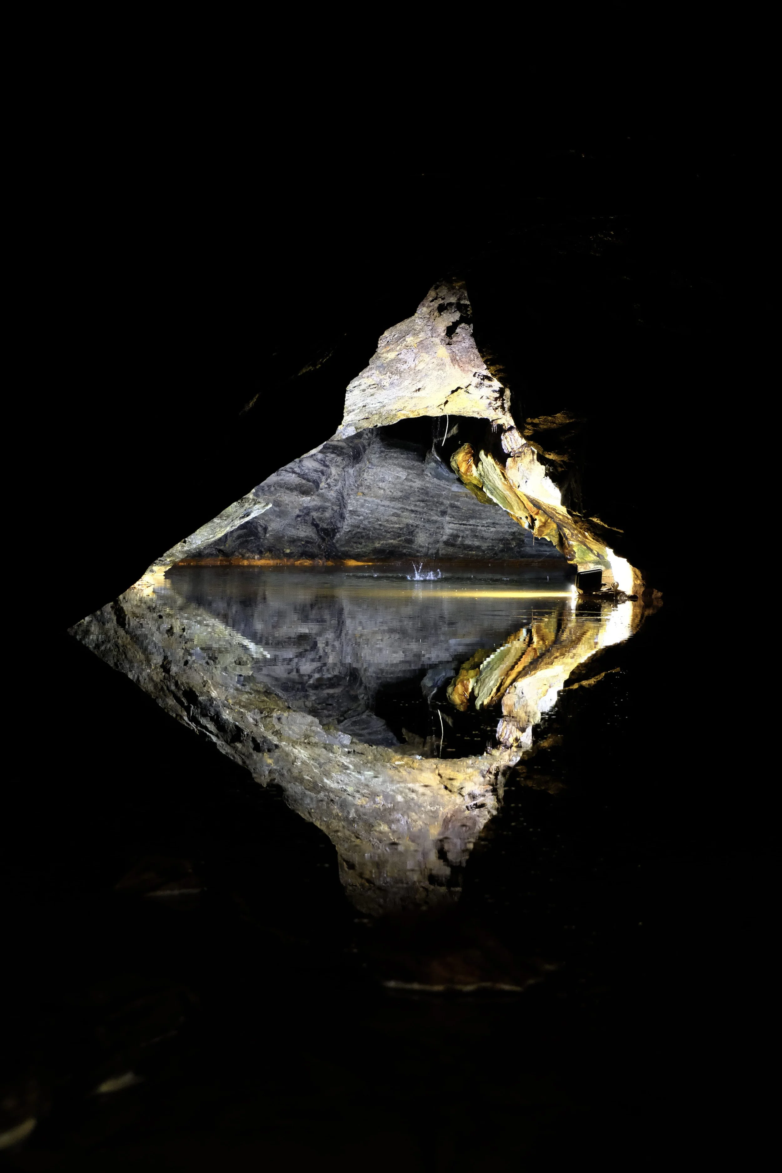Höhlenöffnung mit See und Reflexion auf der Wasseroberfläche, dunkler Umriss der Höhle im Vordergrund.