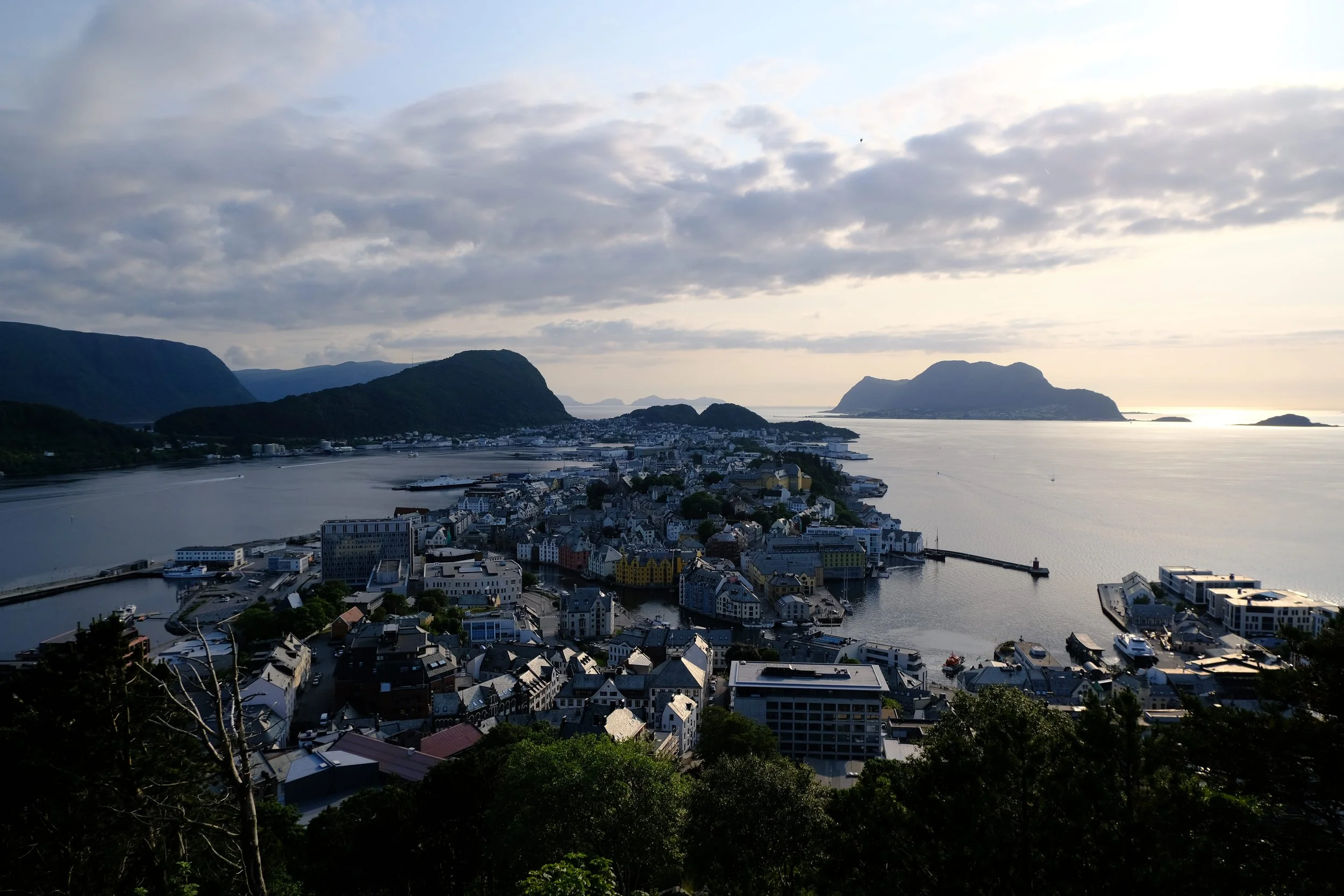 Blick auf eine Küstenstadt mit Wasser, umgeben von Bergen, bei Sonnenuntergang.