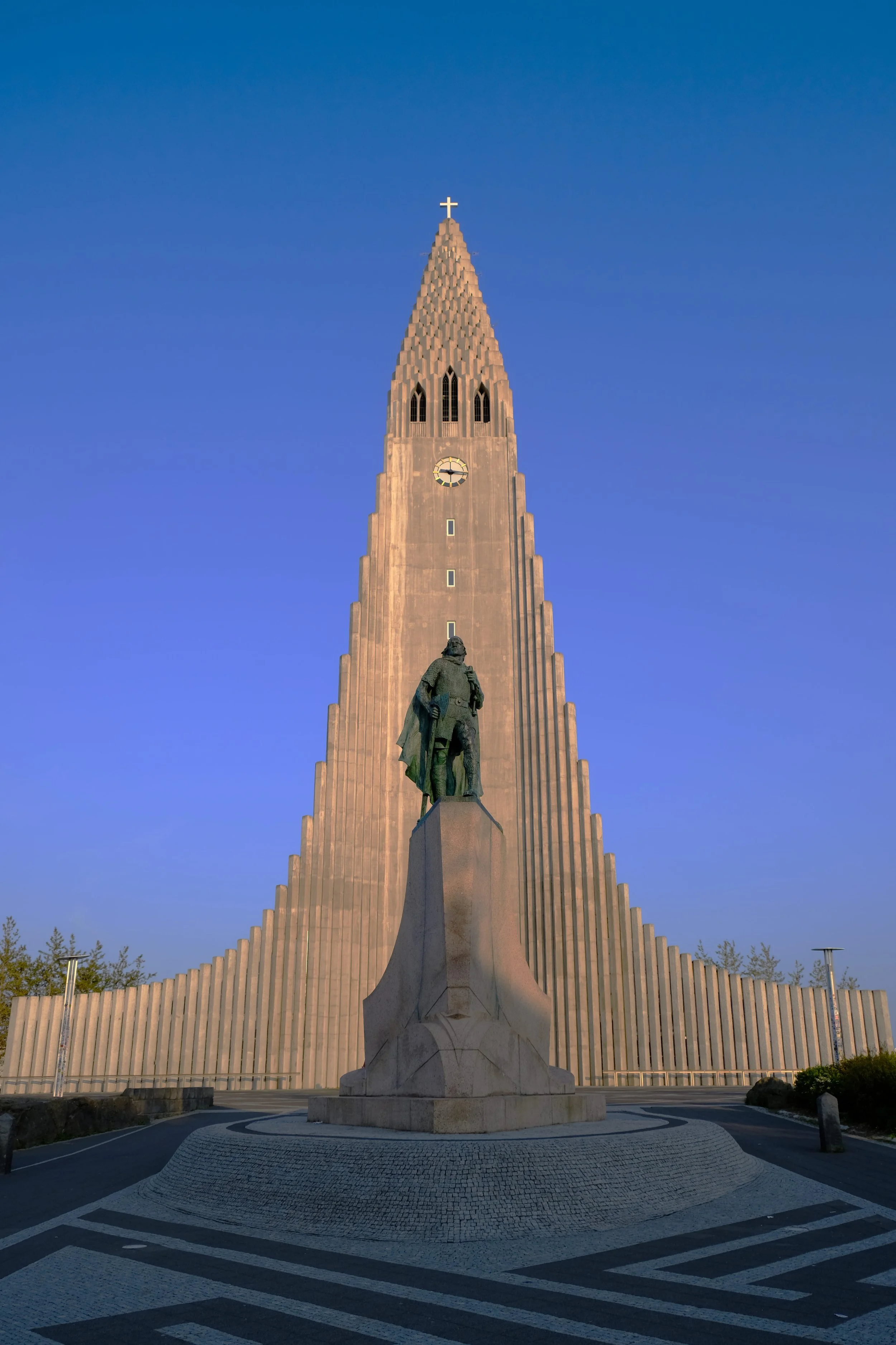 Der Hallgrímskirkja, eine große Kirche in Island, mit einem hellblauen Himmel im Hintergrund. Vor der Kirche steht eine Statue eines Mannes auf einem Steinpodest.