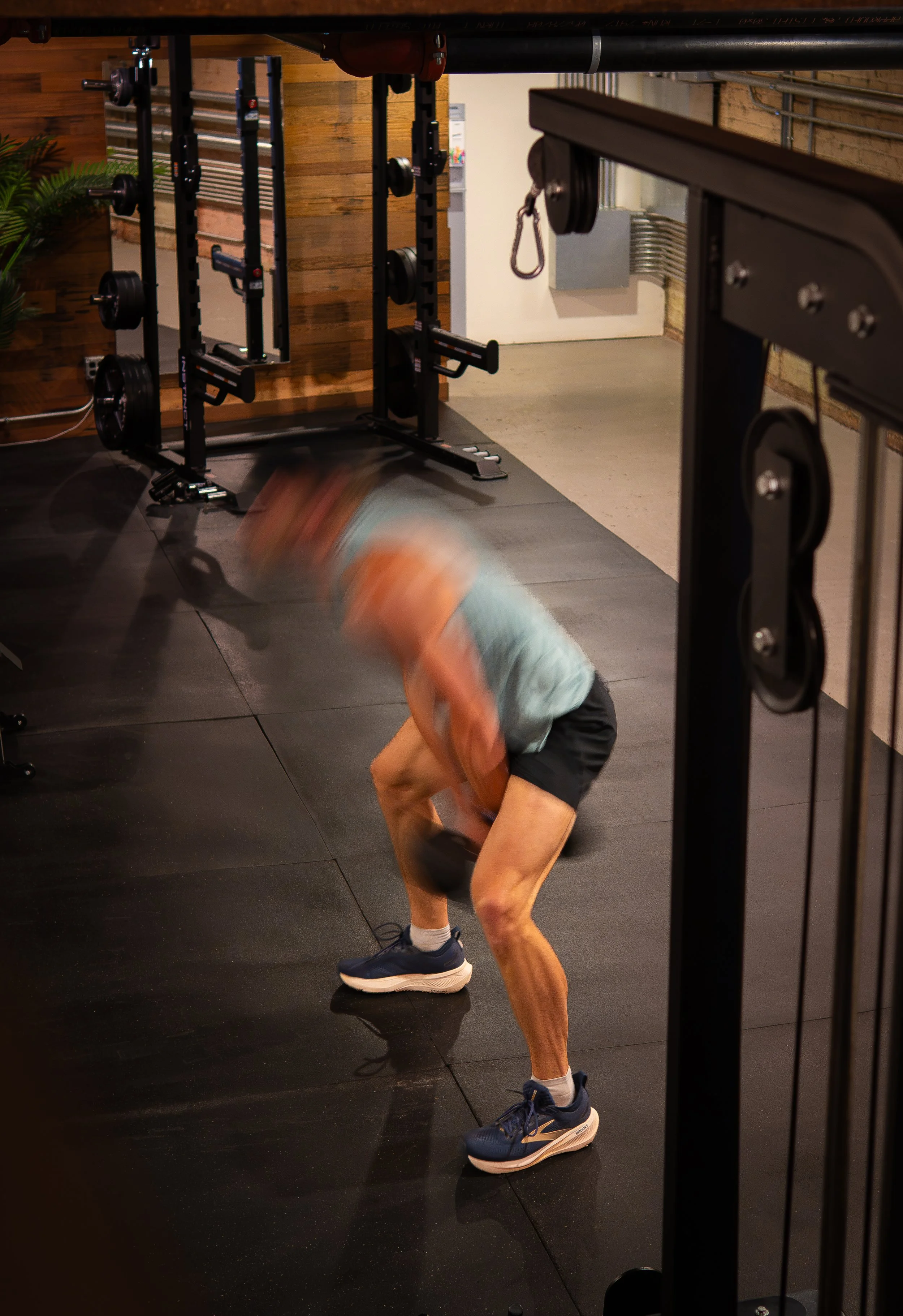A person performing a handstand exercise in a gym, with gym equipment and wooden panels in the background.
