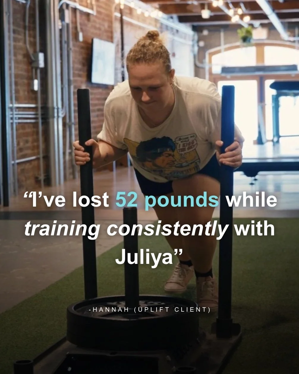 A woman with curly hair in a ponytail pushing a heavy sled on a turf indoor gym with brick walls, graffiti, and exercise equipment, displaying a quote about her weight loss journey.